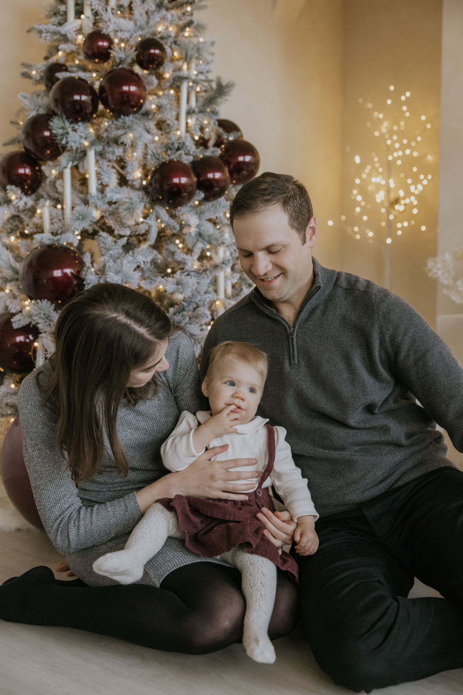A family shares tender moments together while sitting by a decorated Christmas tree with twinkling lights.