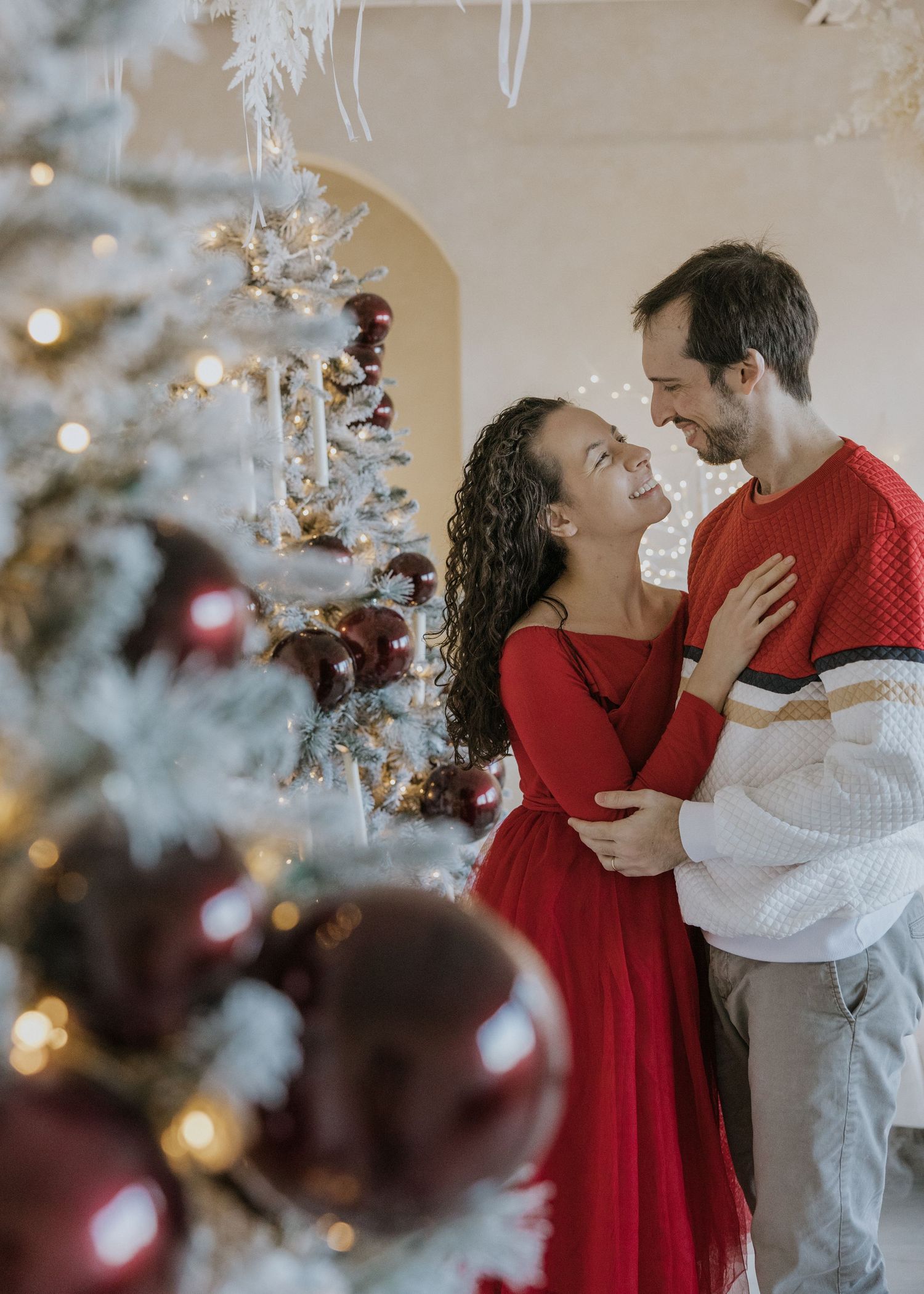 A couple in red and white holiday attire share romantic moments near a decorated Christmas tree.