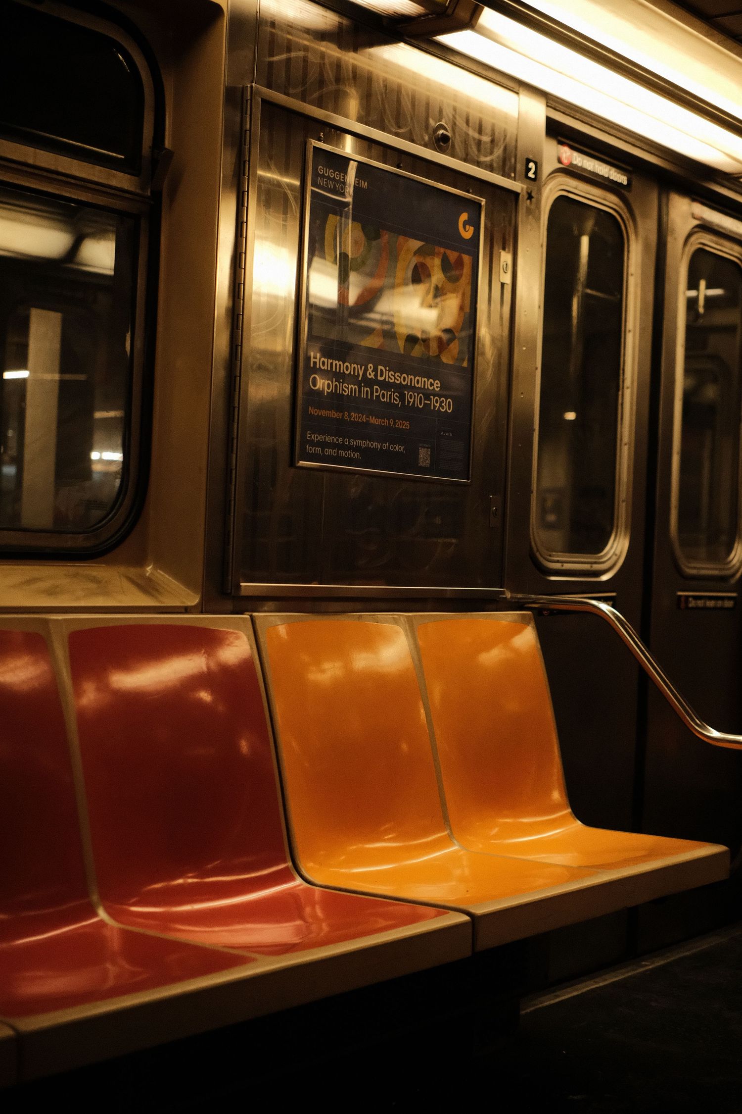 Empty orange subway seats illuminated by overhead lighting in a dark train car.