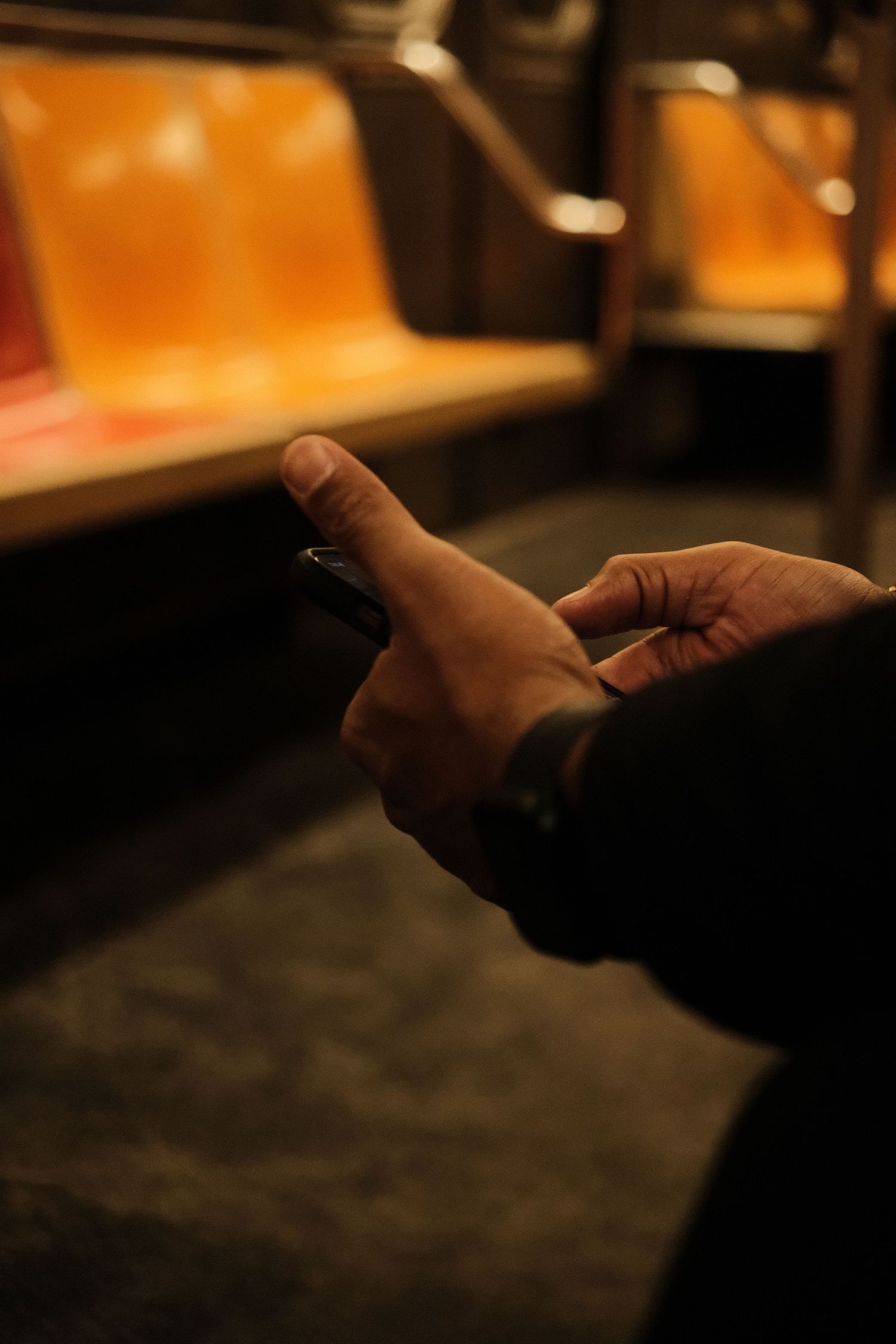 Silhouetted hands holding a device in dimly lit subway car.