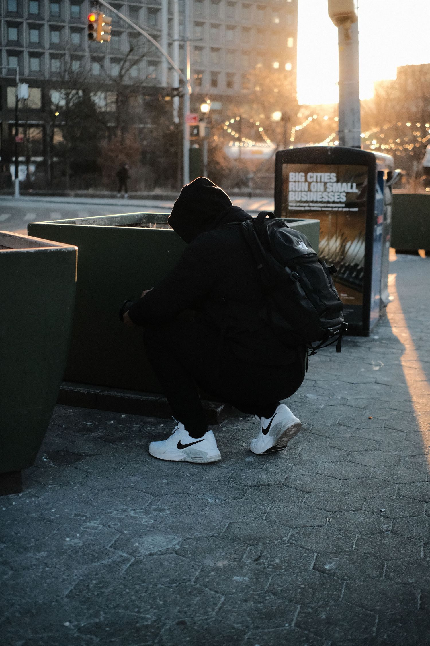Person in dark clothing and Nike shoes sitting against urban backdrop at sunset.