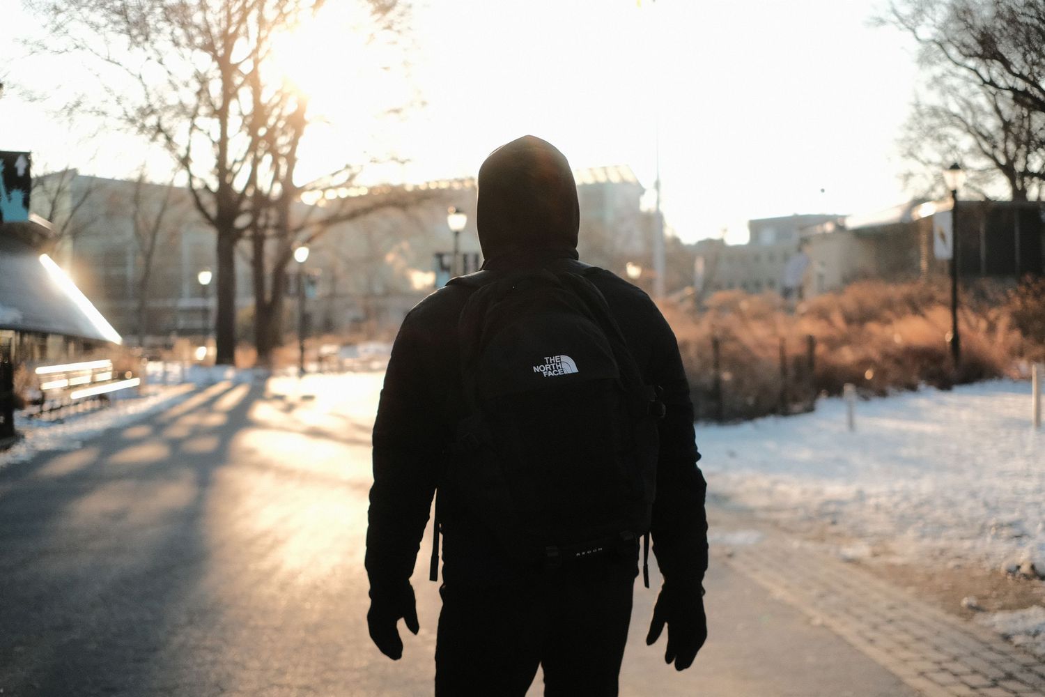 Silhouette of person in North Face jacket walking on winter path at sunset.