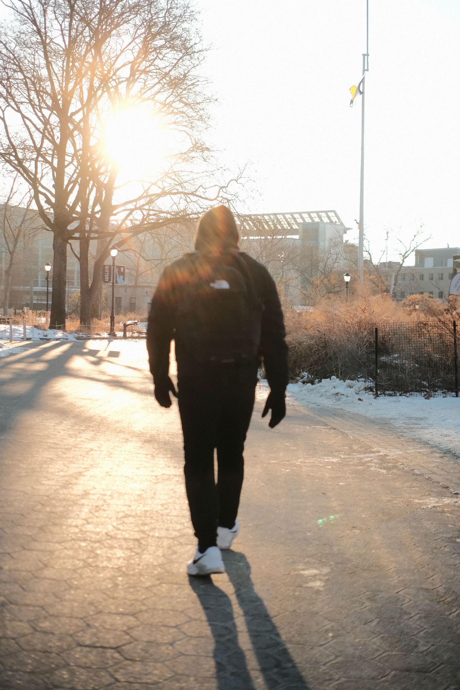 Person in dark winter clothing walking on snowy path during golden hour sunset.
