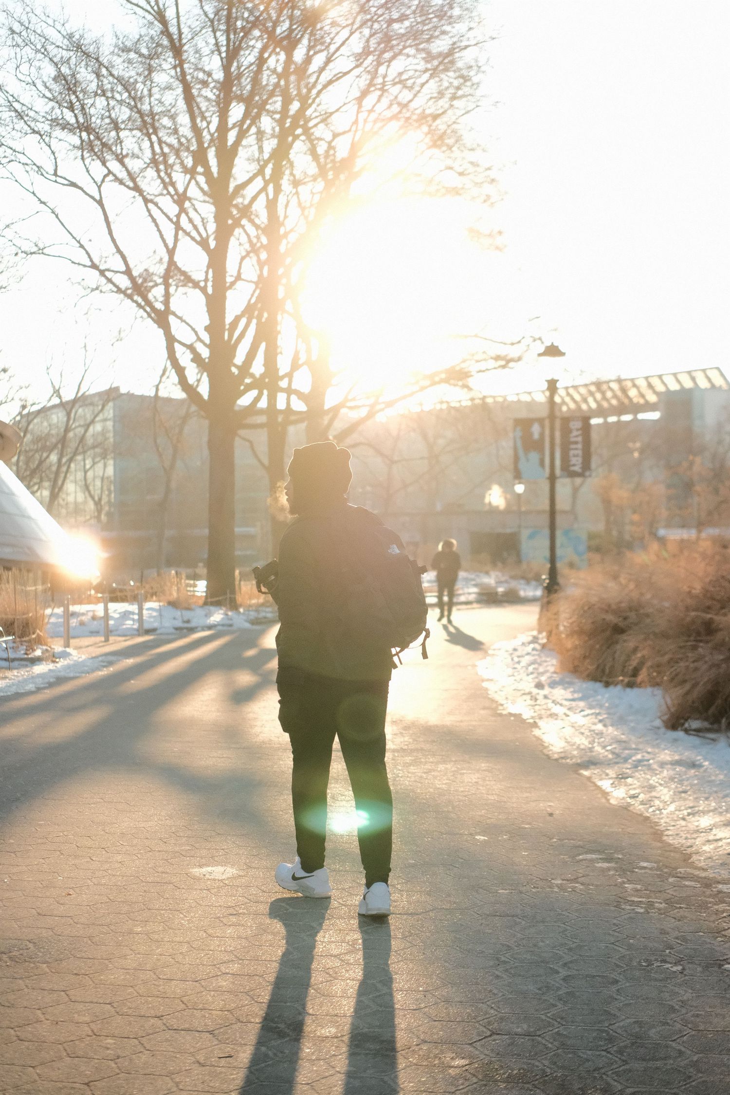 Silhouette of a person standing on snowy path during golden hour sunset.