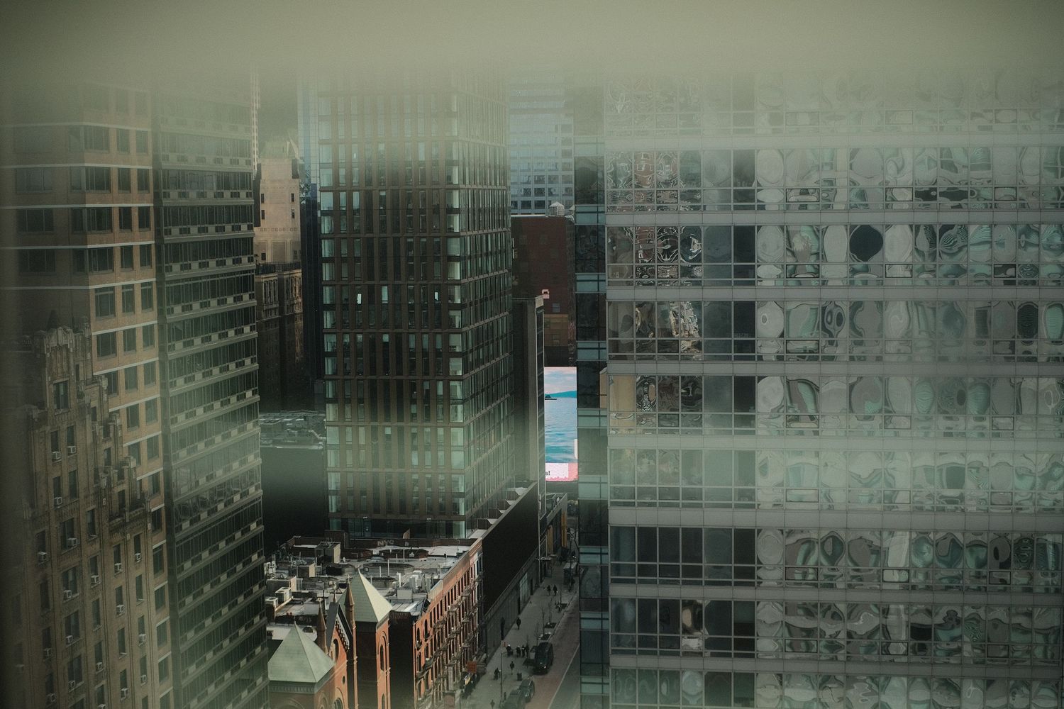 Foggy view of modern glass office buildings through rain-covered window.