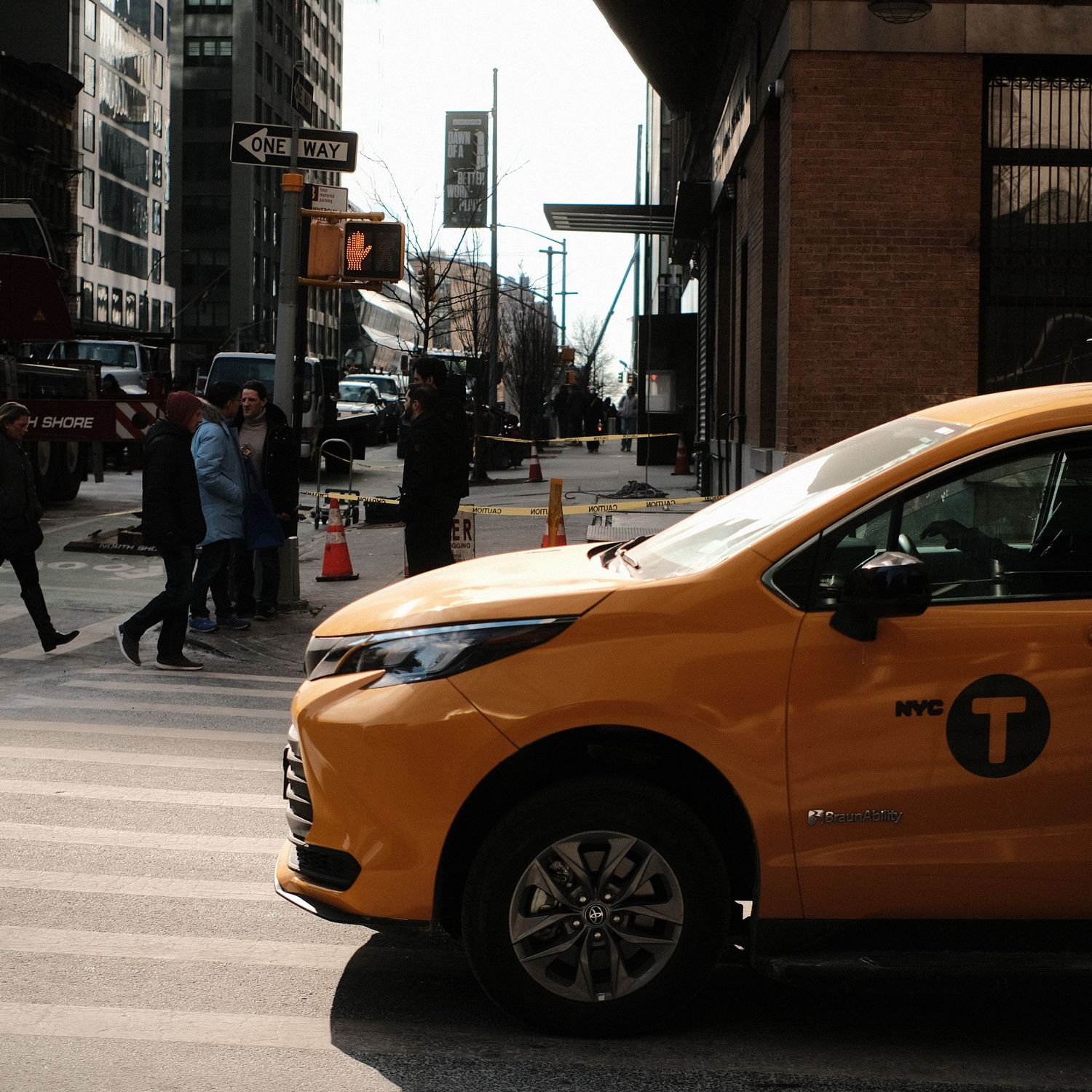 Yellow NYC taxi cab driving on a city street with buildings visible in the background.