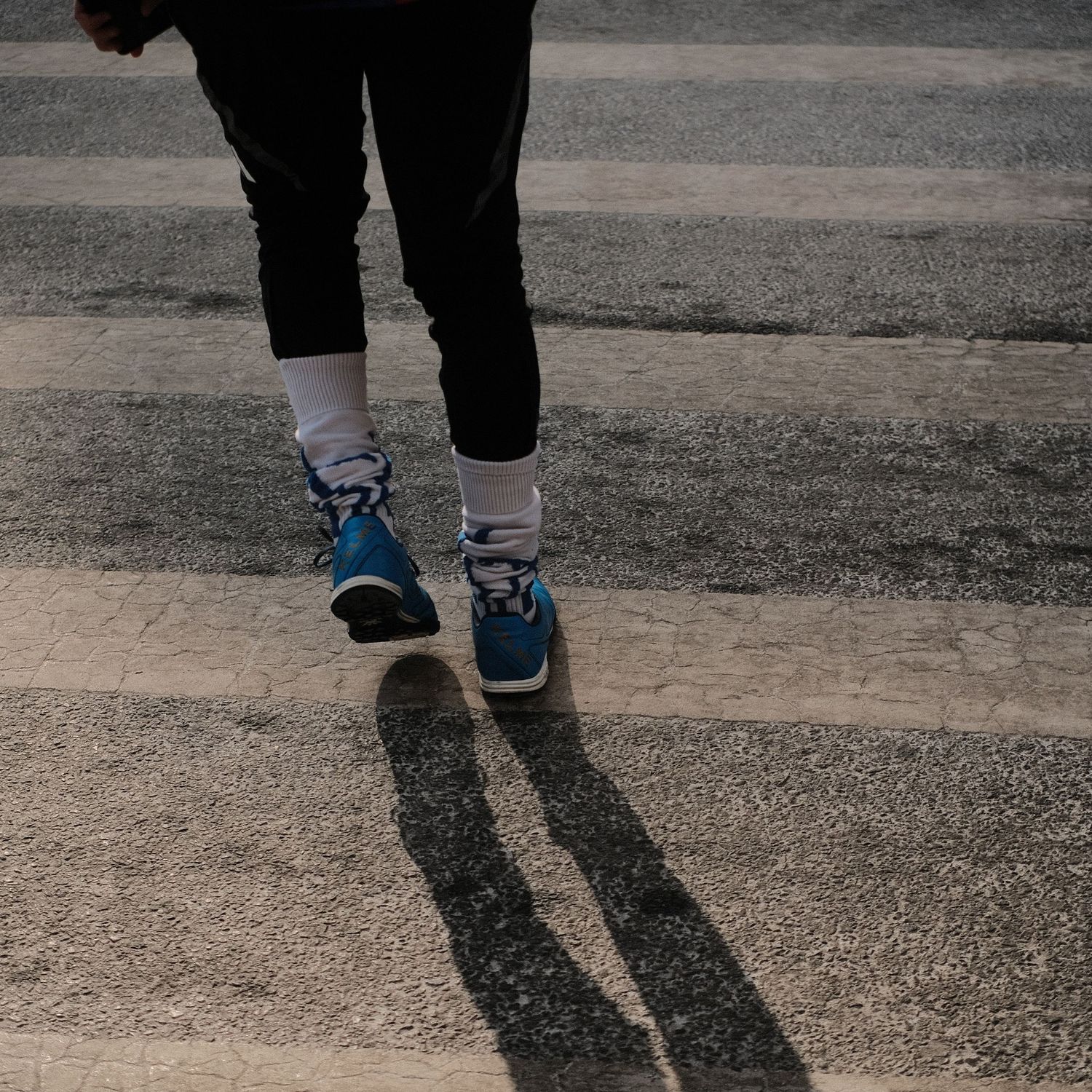 Close-up view of walking feet and shadows cast on concrete sidewalk.