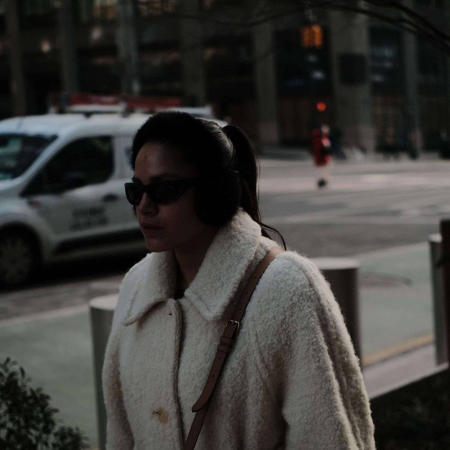 People walking along an urban street with parked cars and buildings in background.