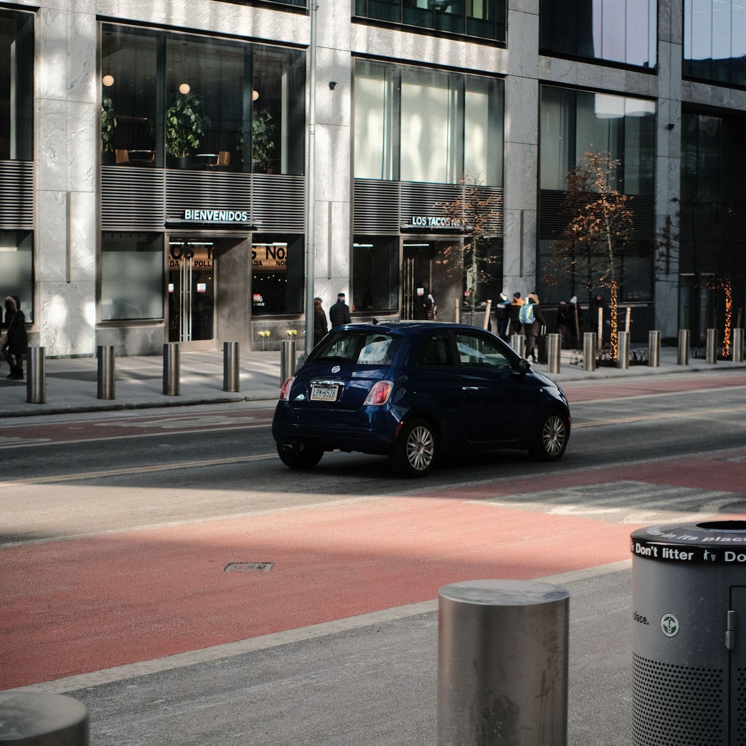 Modern glass office building entrance with concrete bollards and pedestrian walkway.