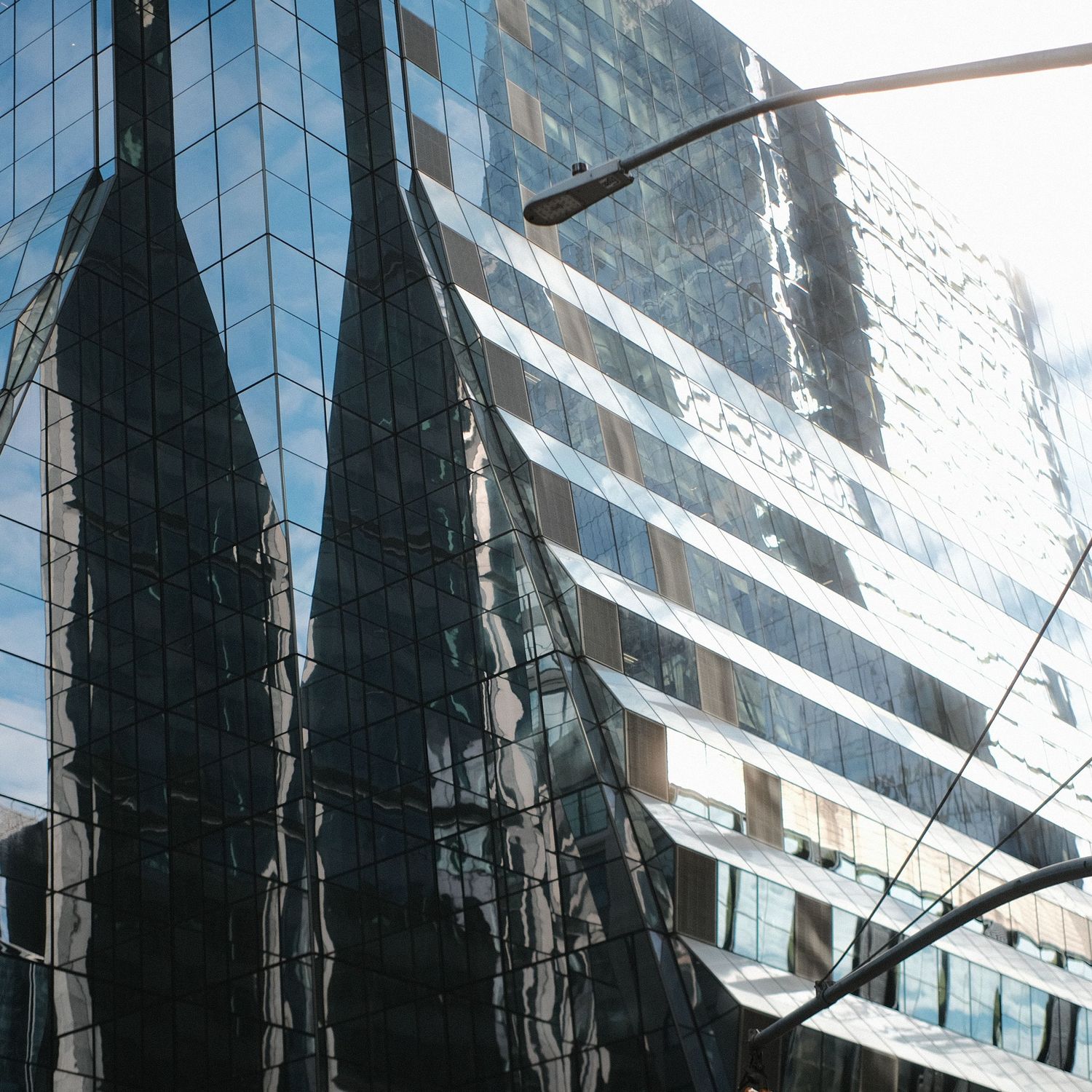 Modern glass office building with reflective facade creating geometric patterns against blue sky.