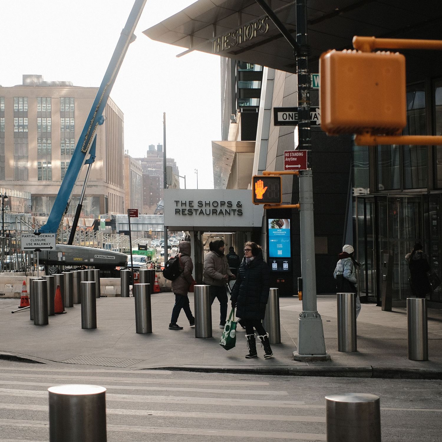 Urban street corner with traffic signal and restaurant entrance surrounded by construction barriers.