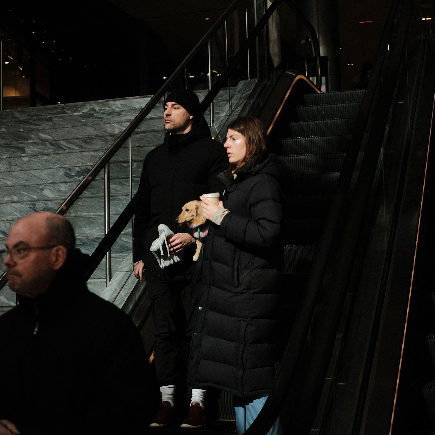 People riding an escalator inside a modern building with marble walls and metal railings.
