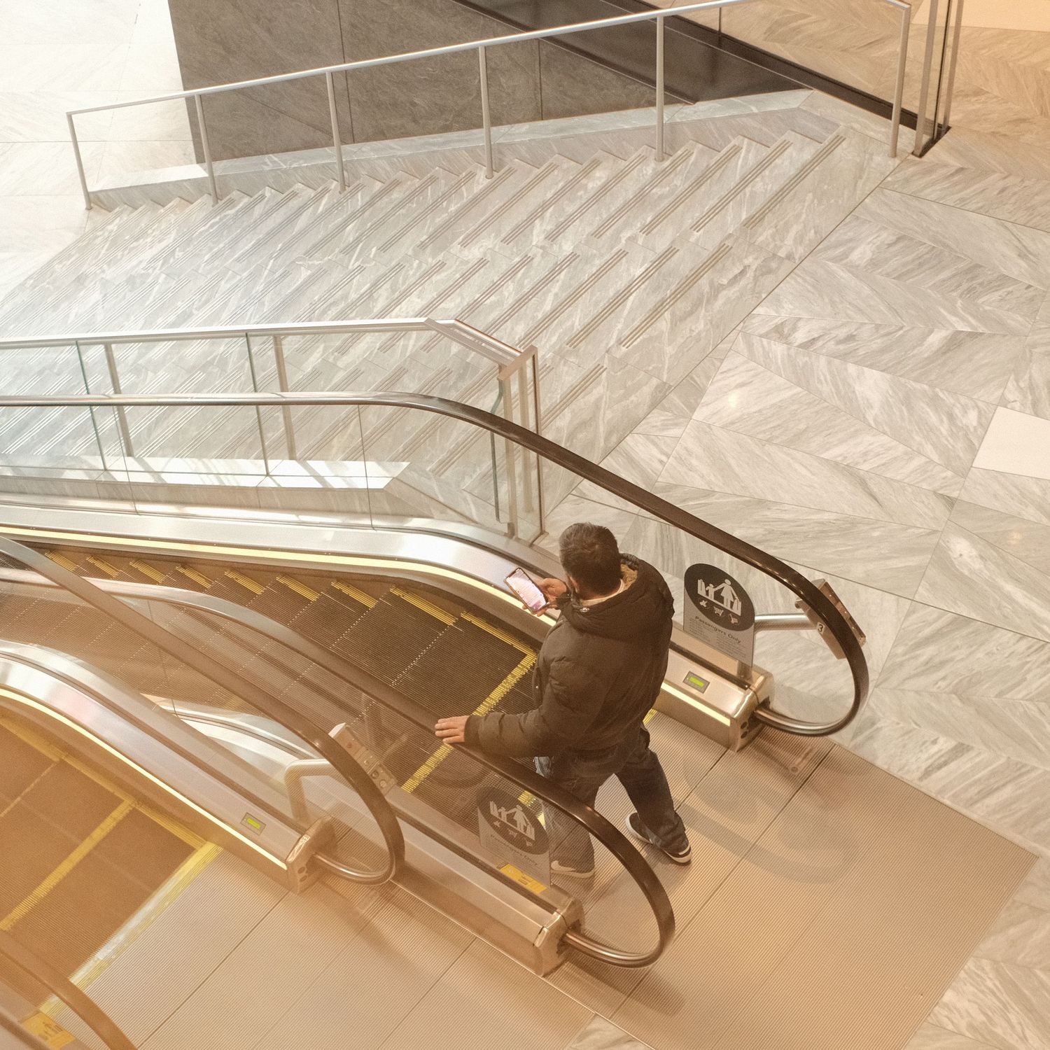 Person riding down an escalator in a modern building with chevron-patterned marble floors.