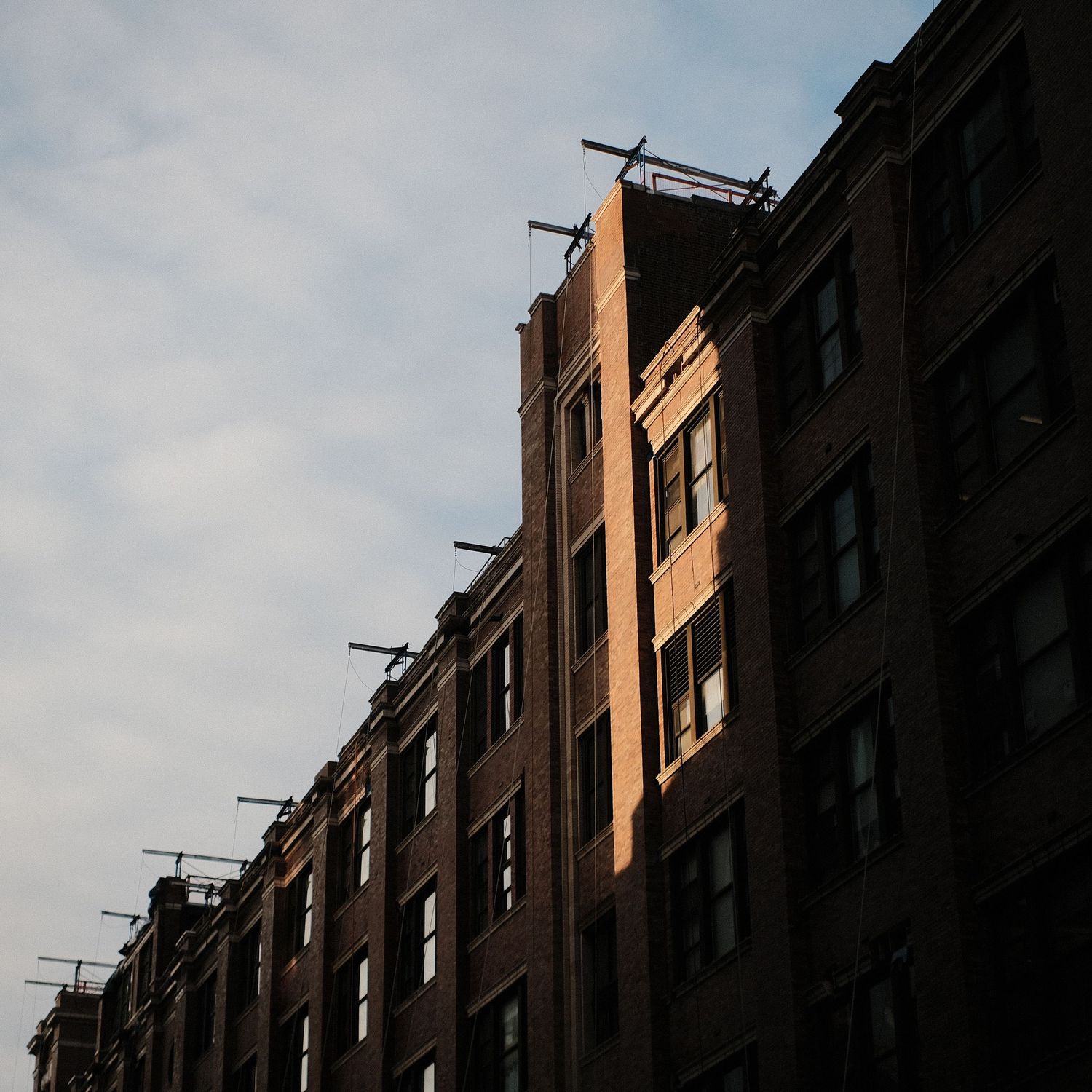 Brick apartment building facade at sunset with fire escapes casting dramatic shadows.