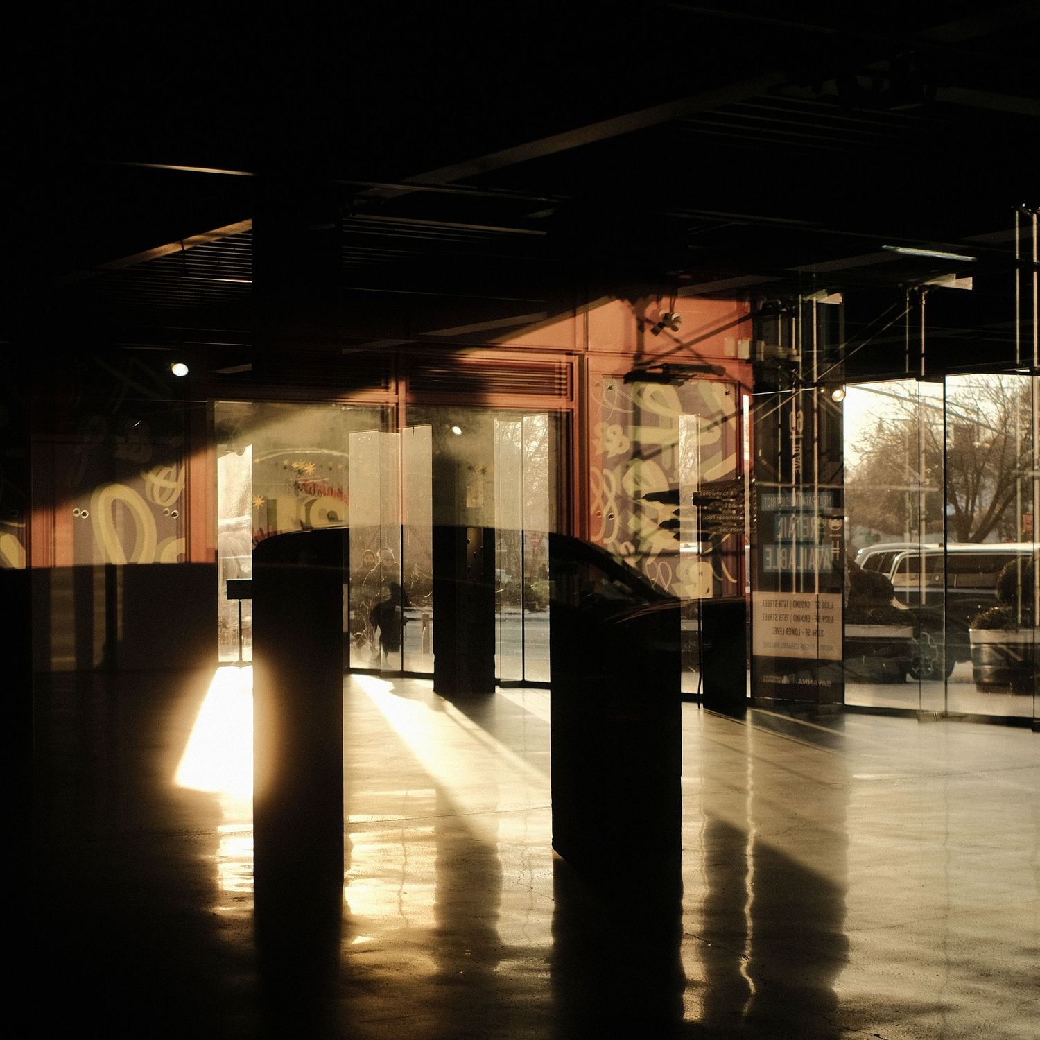 Sunlight streams across a dark empty indoor space creating dramatic shadows on the floor.