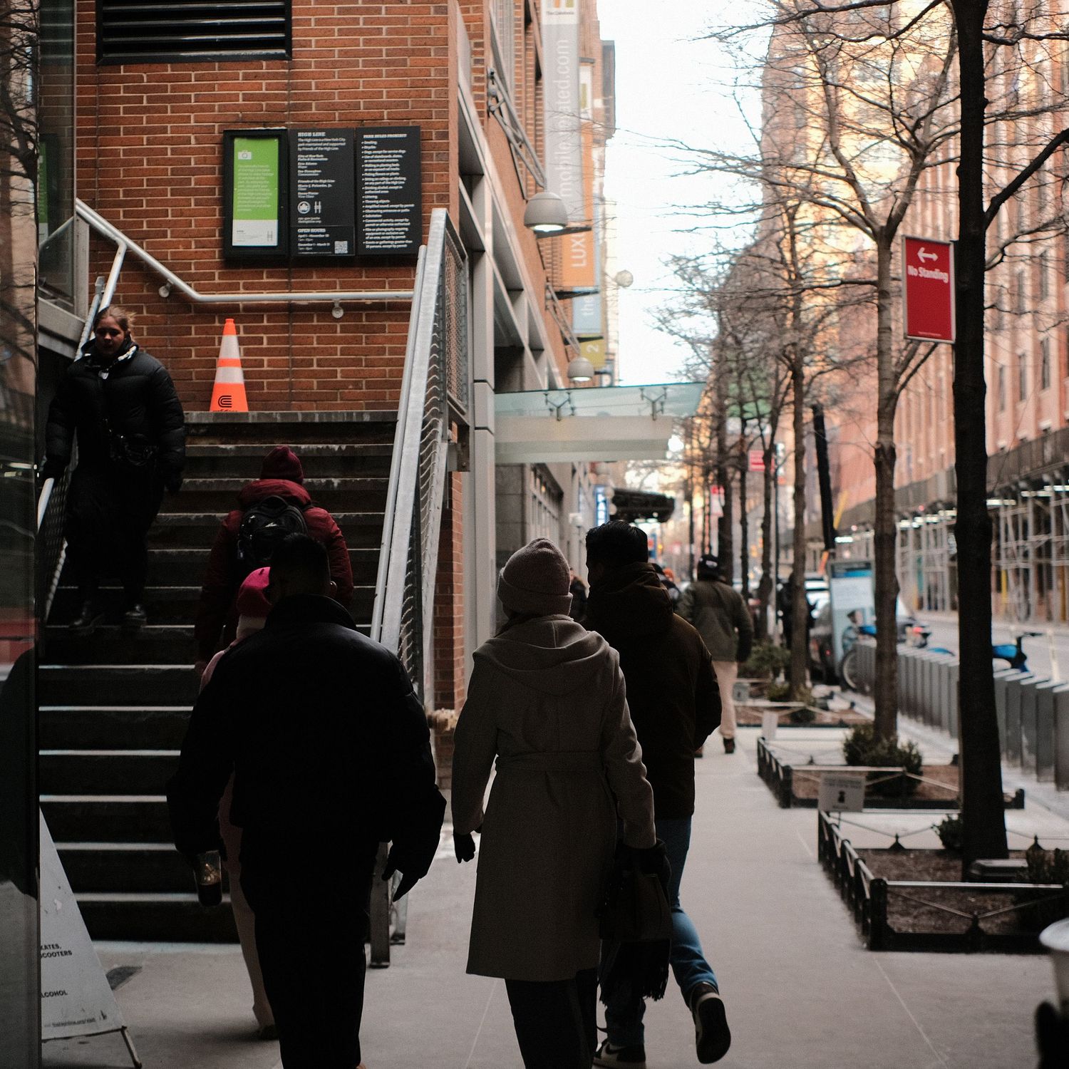 People walking along an urban sidewalk with brick buildings and stairs in winter.
