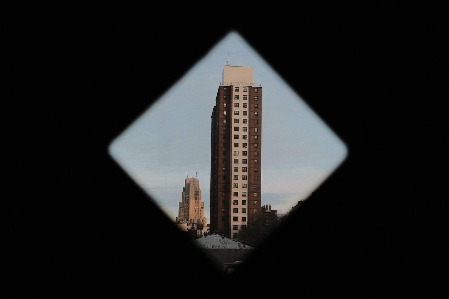 Tall brick building viewed through a diamond-shaped frame against blue sky.