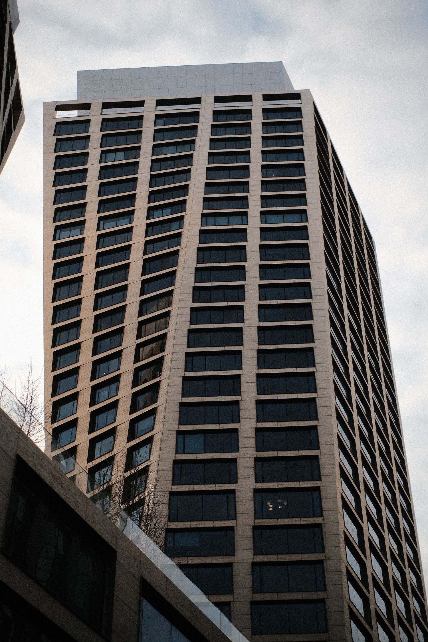 Modern office building with geometric glass windows and concrete facade against cloudy sky.
