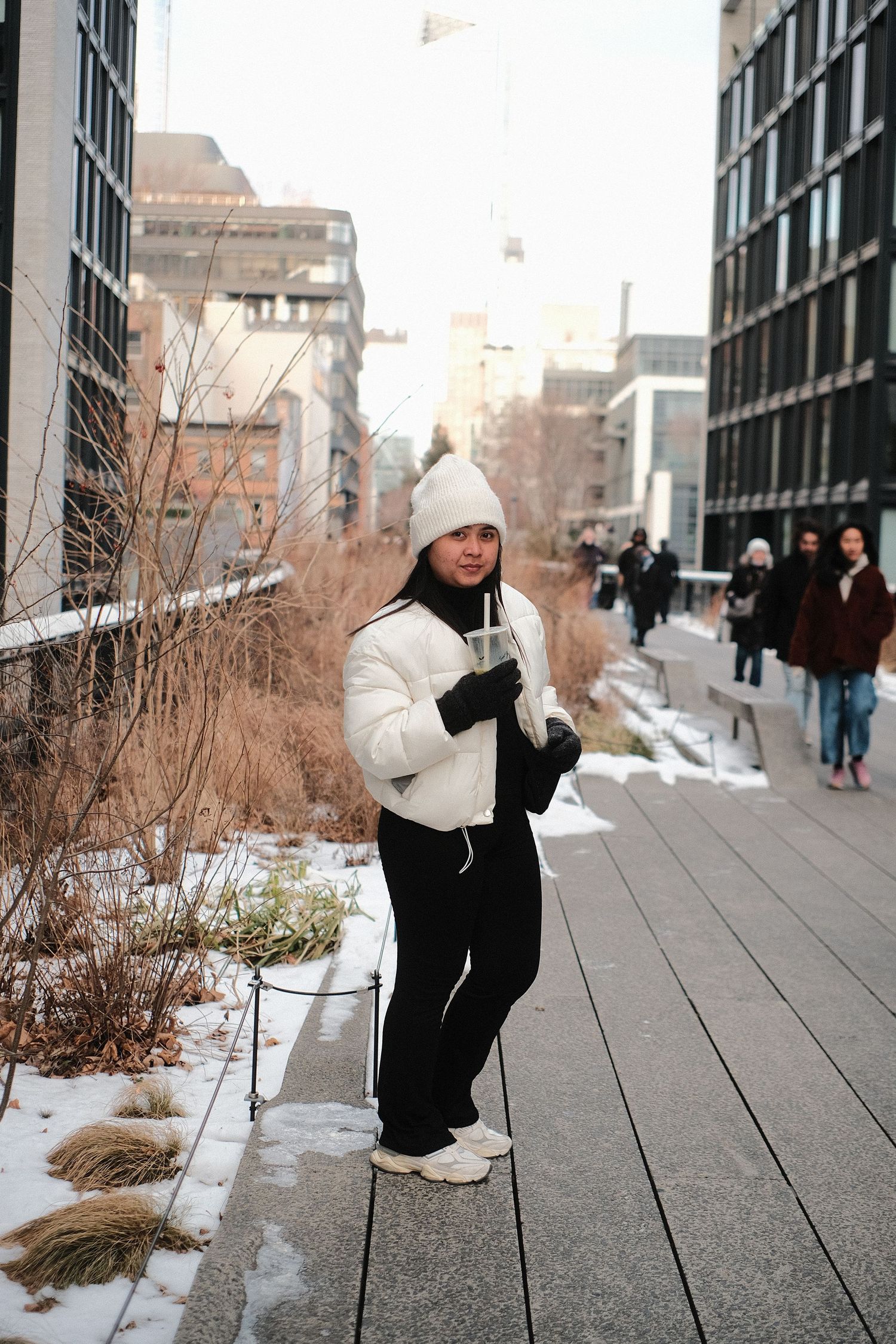 Person in white winter clothing crouching on wooden boardwalk of urban elevated park.