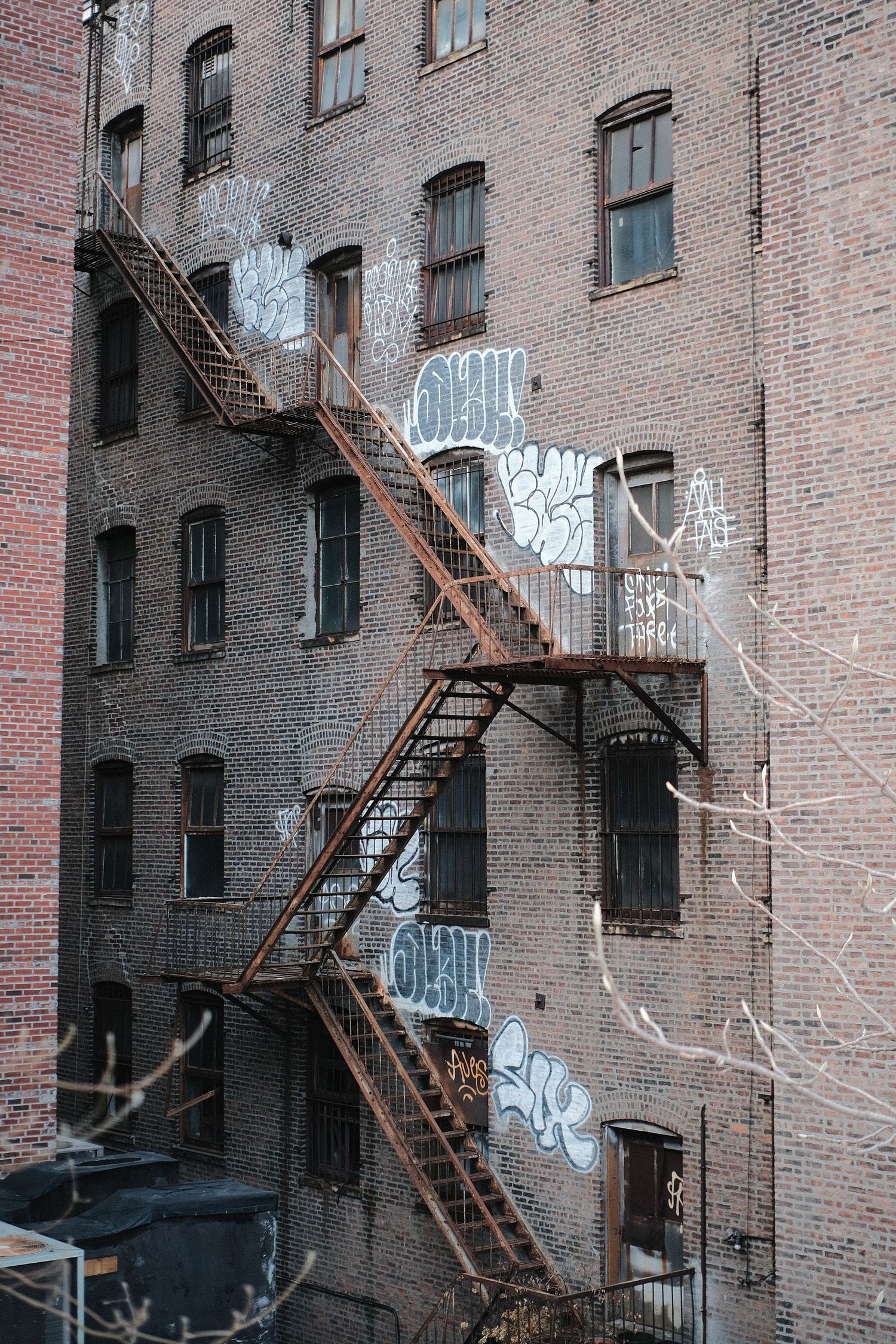 Old brick building with fire escapes and graffiti on exterior wall.