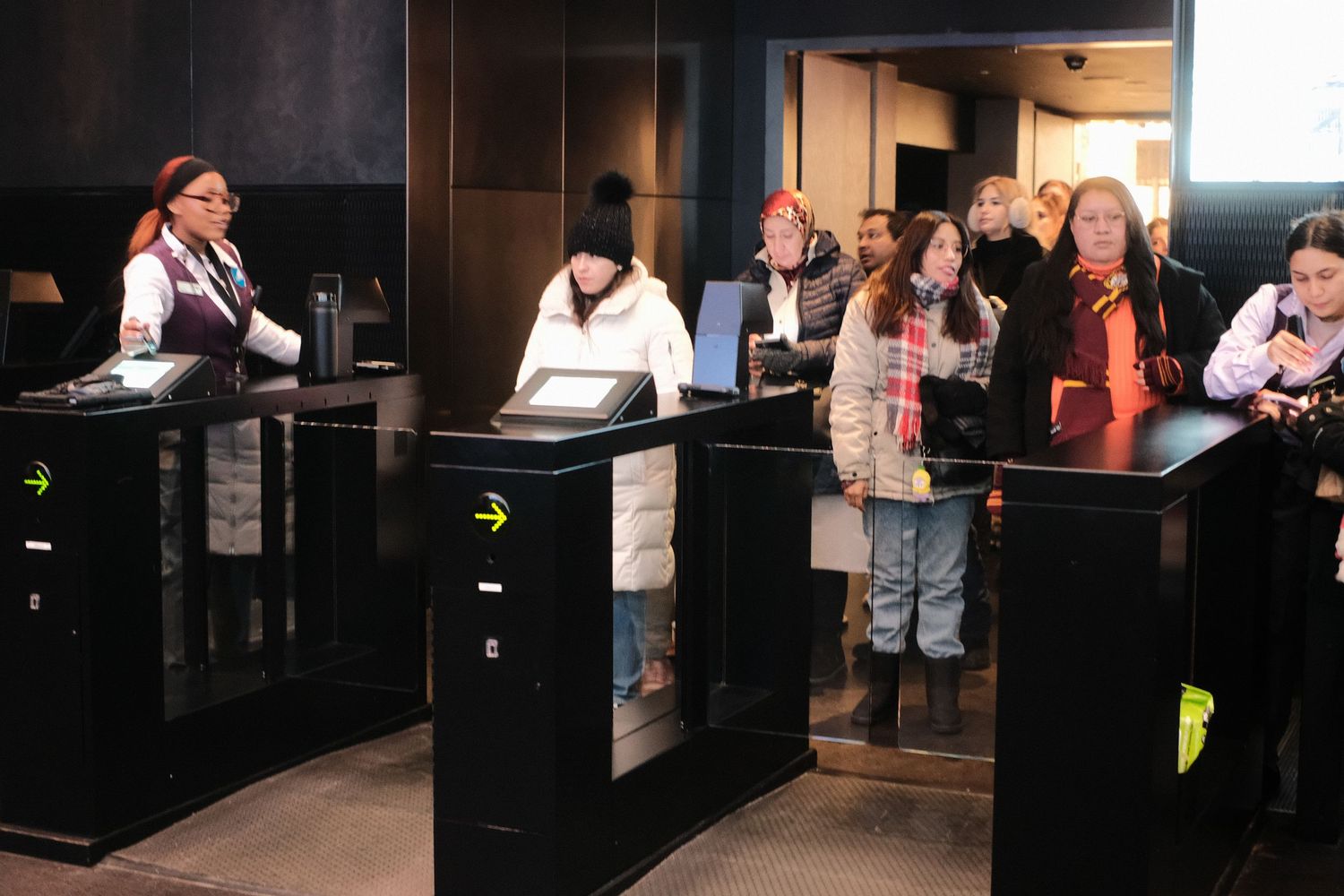Interior of a dark venue with people waiting in line behind stanchion barriers.