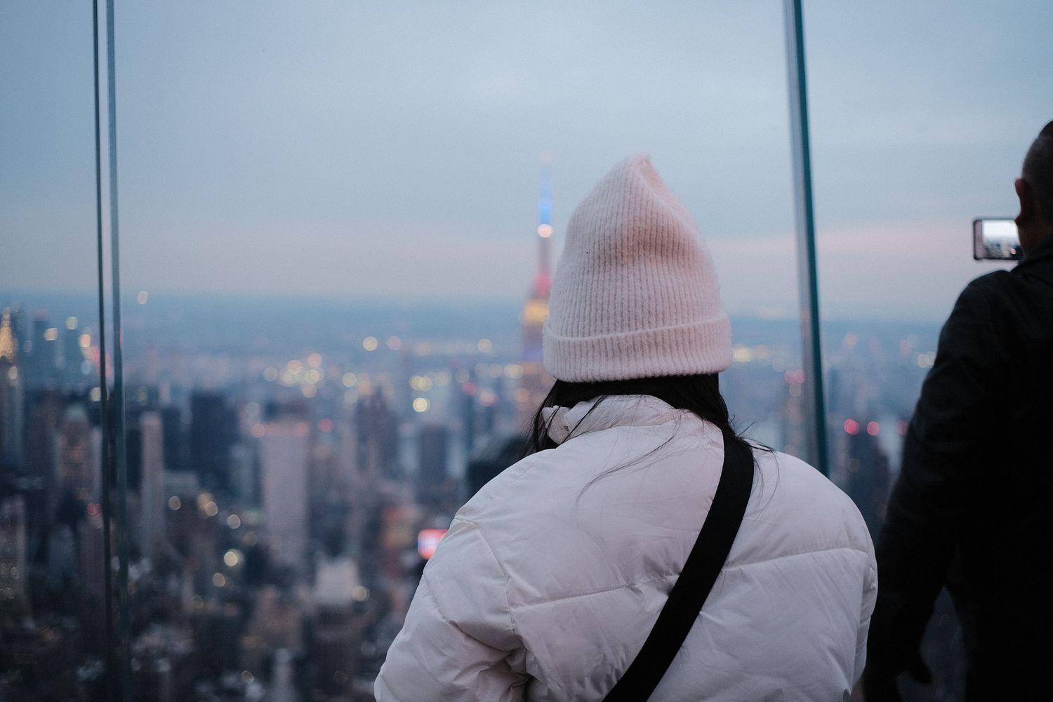 Observation deck visitors looking out at New York City skyline during sunset.
