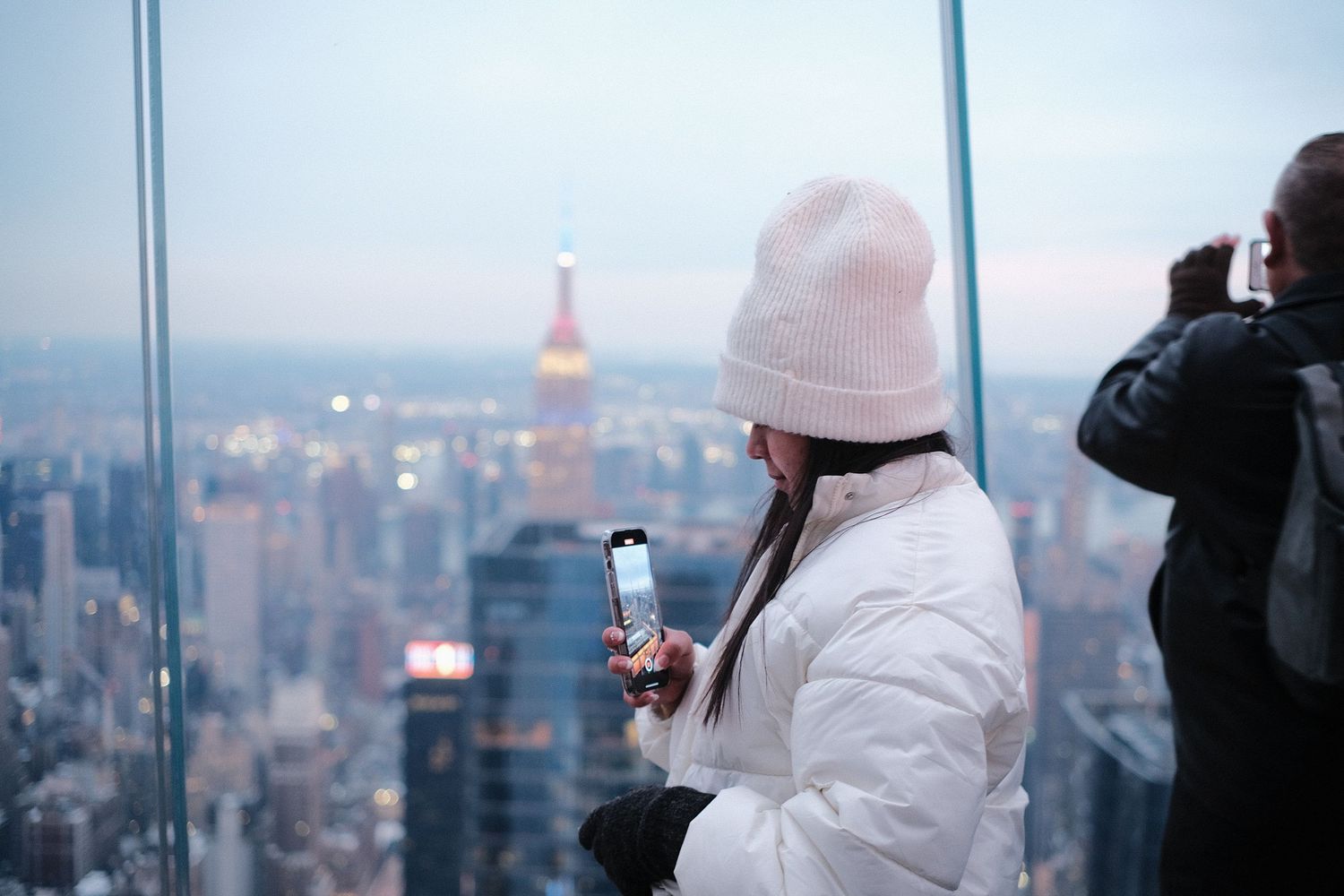 Visitors in winter clothing viewing Manhattan skyline from observation deck.