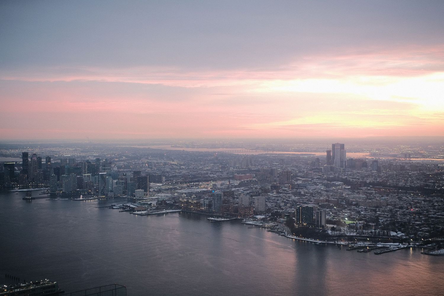Dramatic cityscape view of Manhattan's skyline and harbor during golden hour.