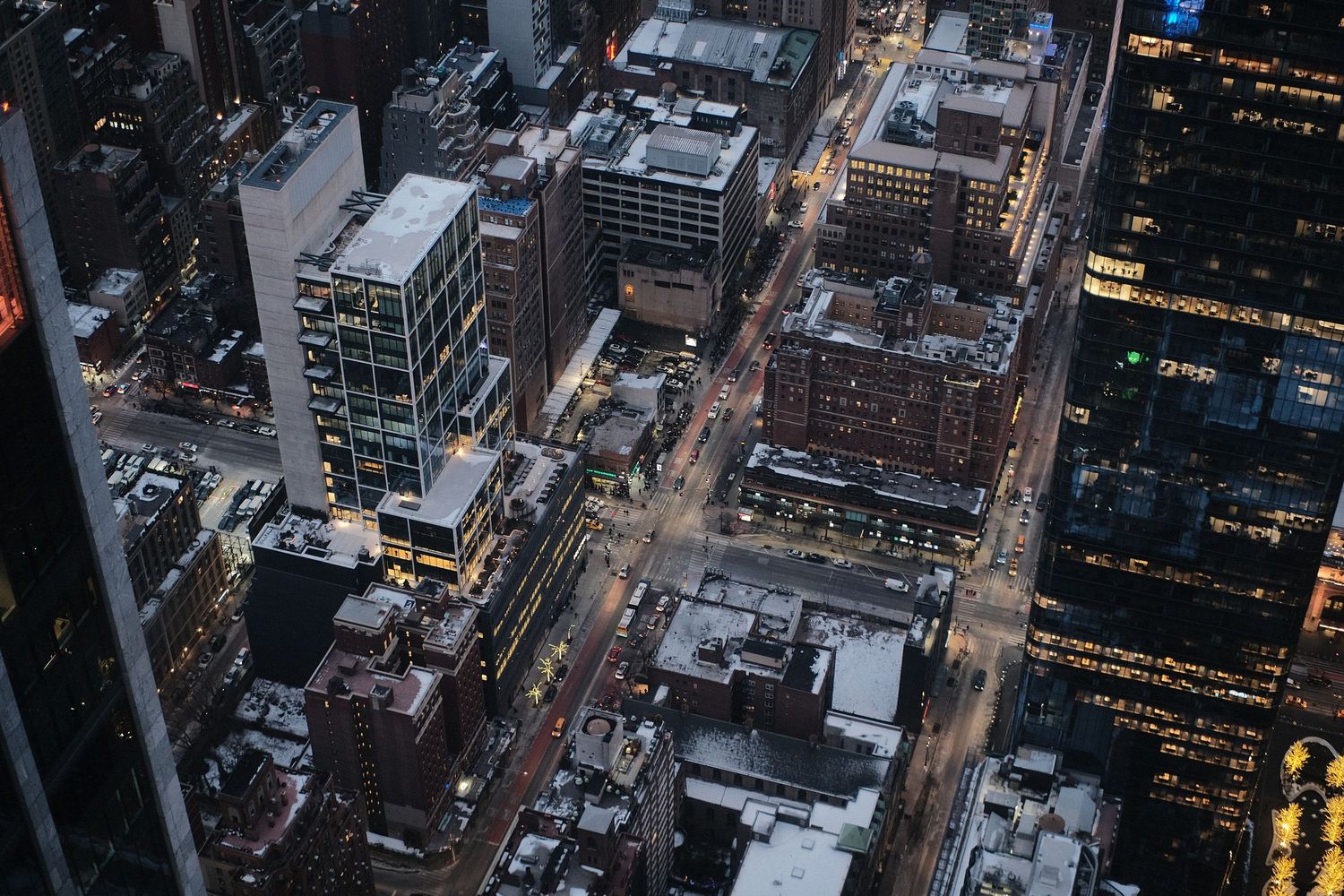 Overhead view of city streets and buildings with glowing lights at night.