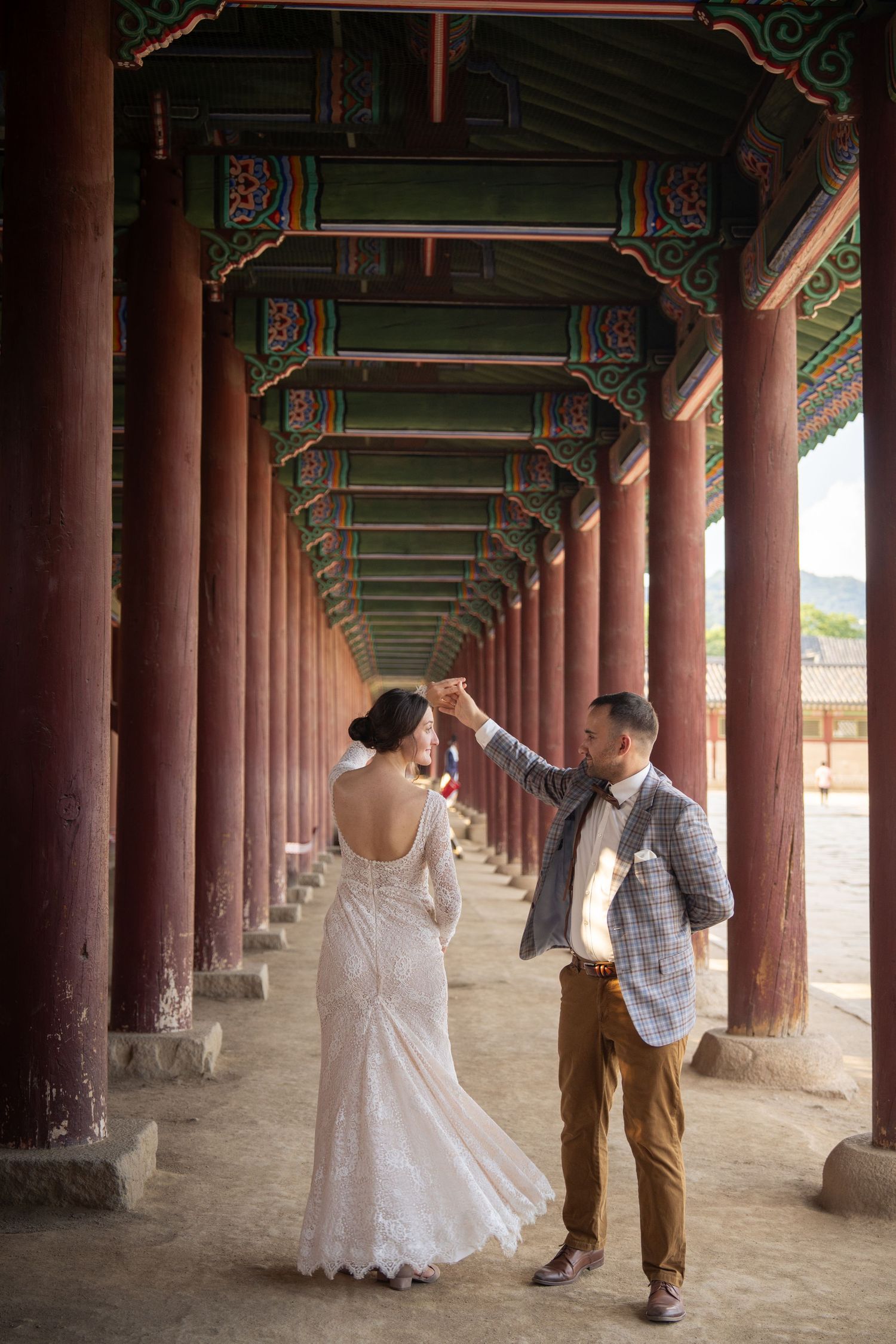 A couple shares a romantic moment under a traditional Korean palace corridor with wooden pillars and ornate architecture.