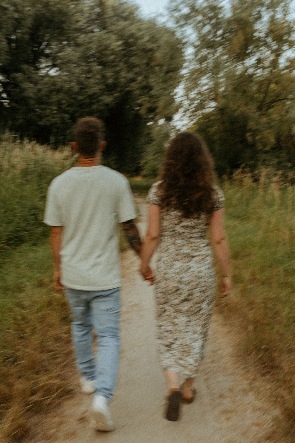 Couple walking hand in hand on a nature path during golden hour.