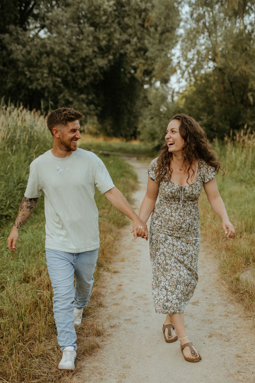 Joyful couple laughing while walking together on a dirt path surrounded by tall grass.