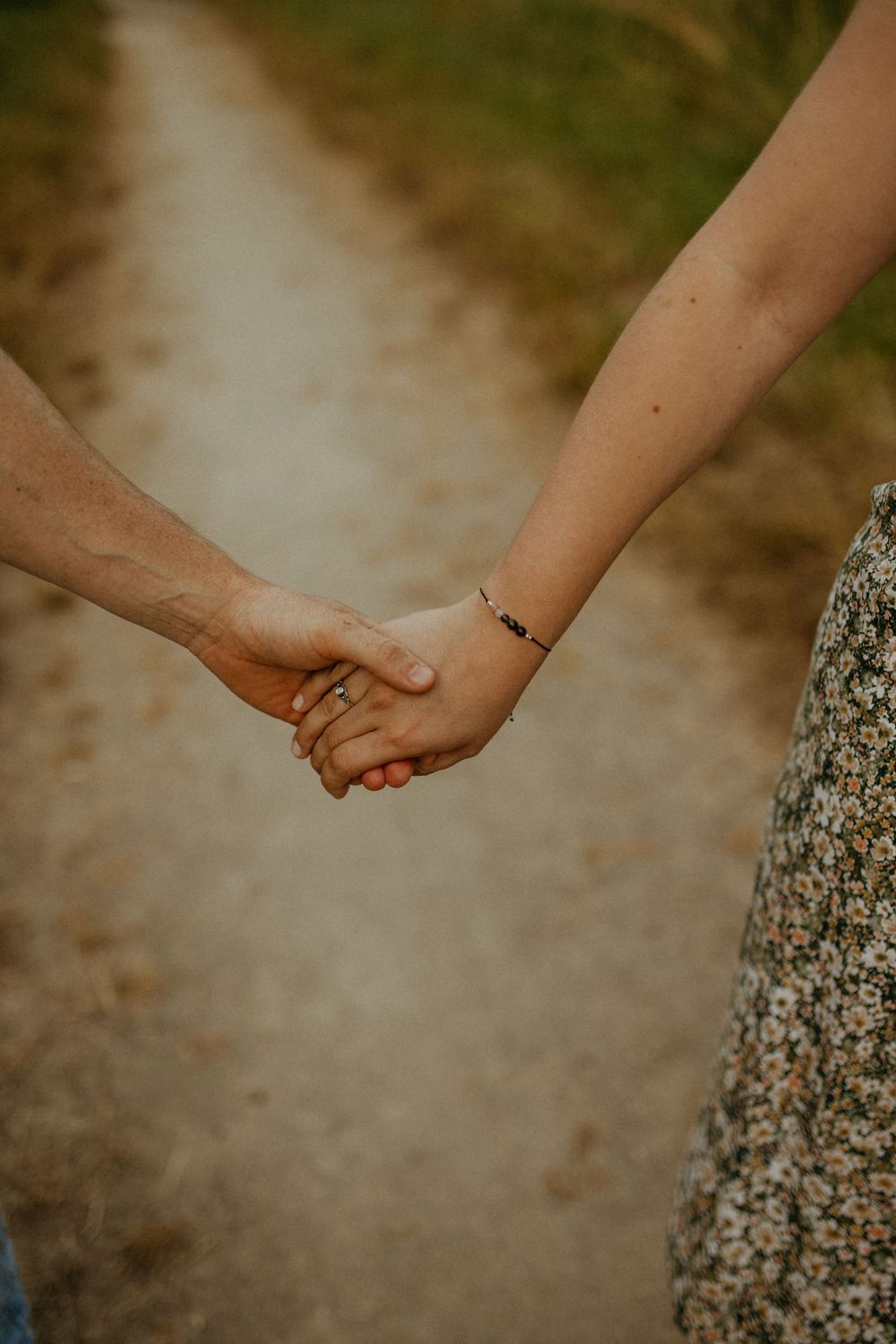 Close-up shot of two hands clasped together on a sunlit path.
