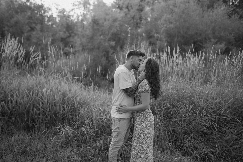 Intimate black and white portrait of a couple embracing in tall grass.
