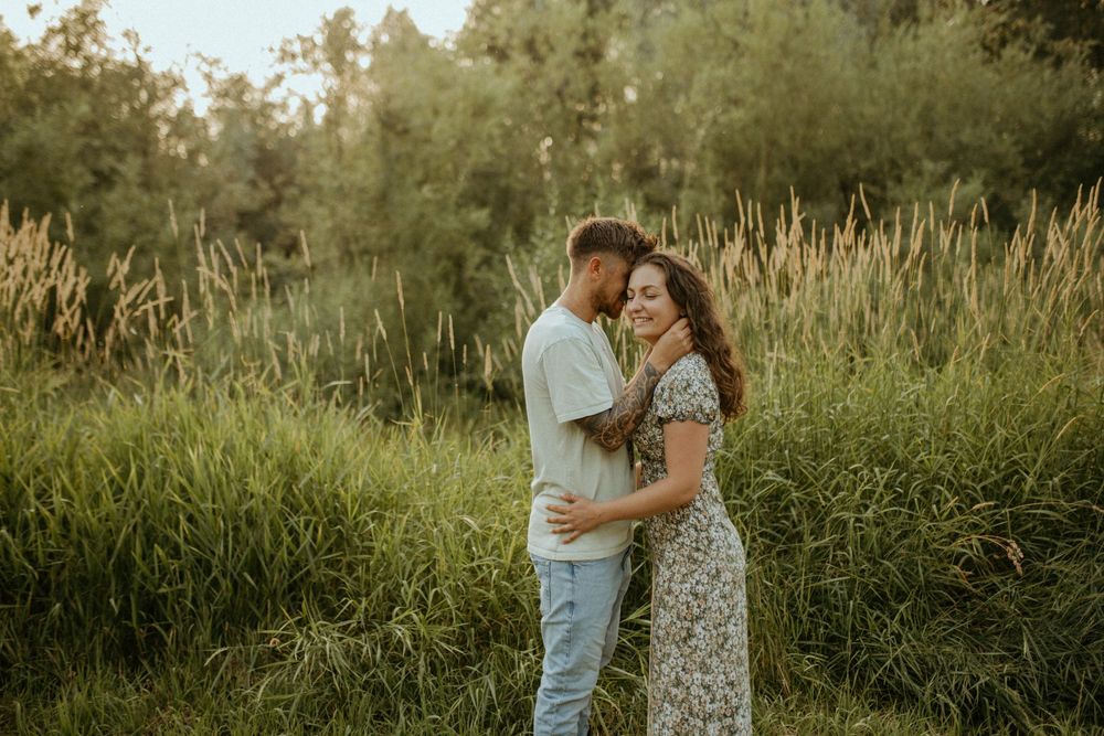 Romantic couple embracing in a sunlit field surrounded by tall grass.