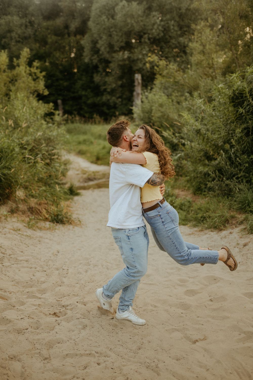 Playful sequence of a couple spinning and dancing on sandy ground surrounded by trees.