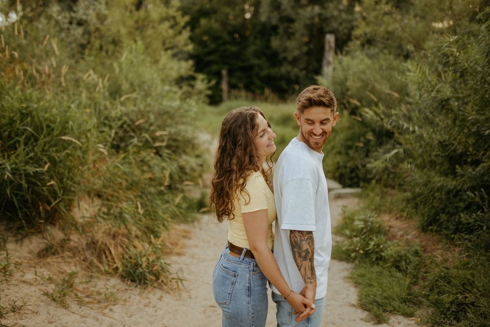 Couple walking hand in hand along a sandy nature path with green foliage.