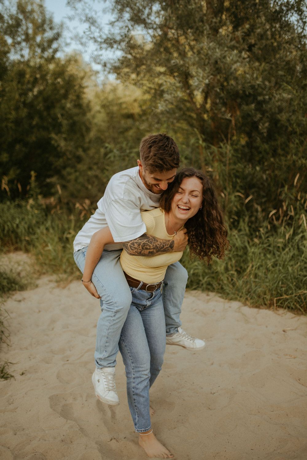 Playful piggyback ride moment captured on a sandy path with natural greenery backdrop.