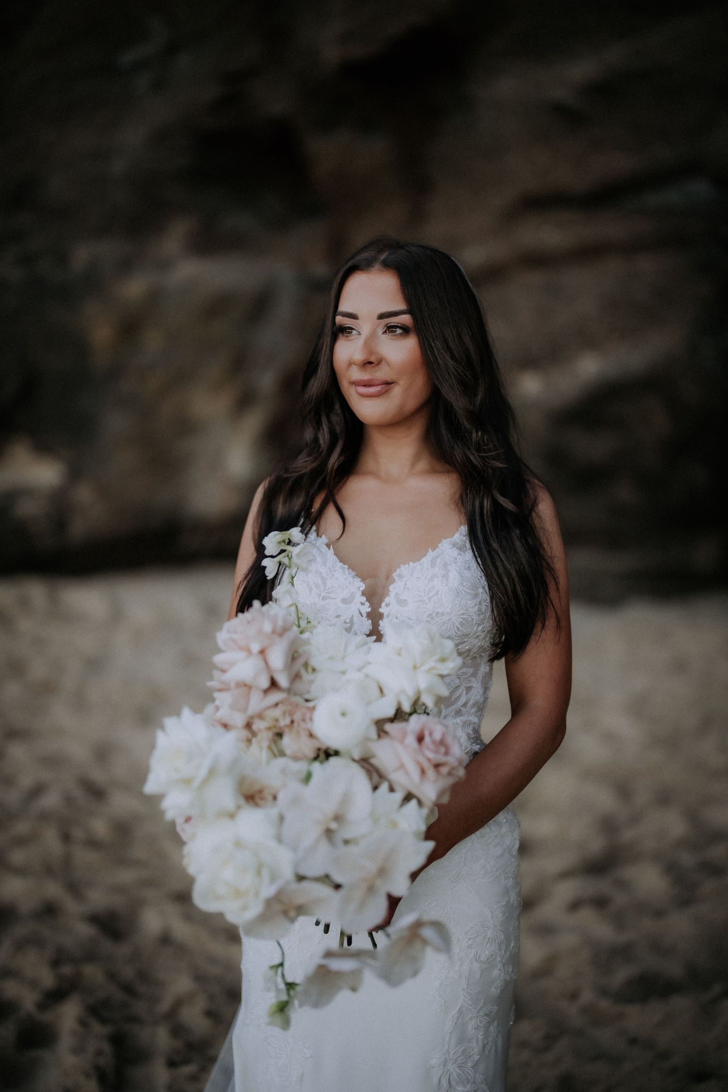A bride holds an elegant white orchid bouquet against a rocky backdrop.