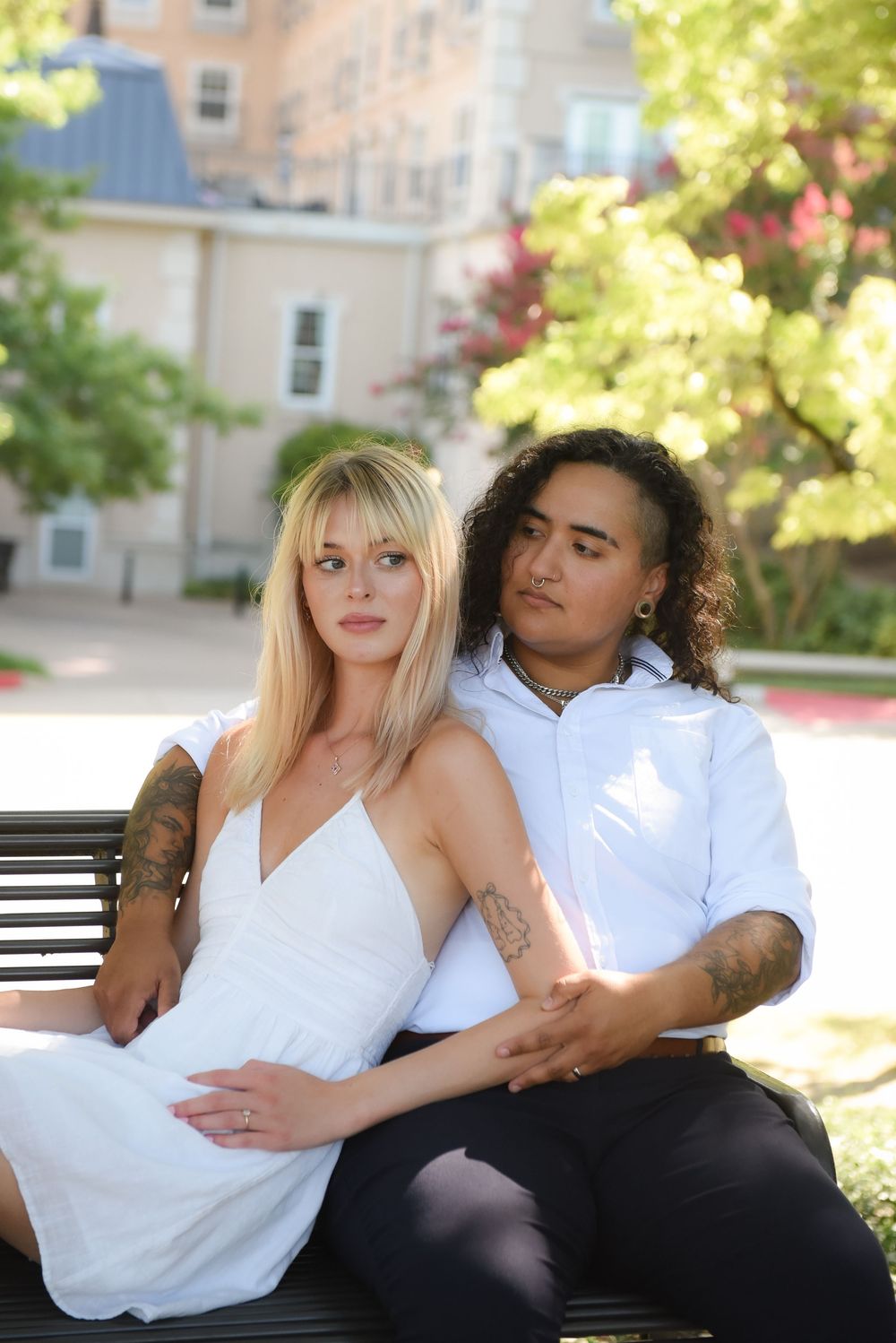 Couple in coordinated white outfits relaxing on outdoor bench in sunlit garden.