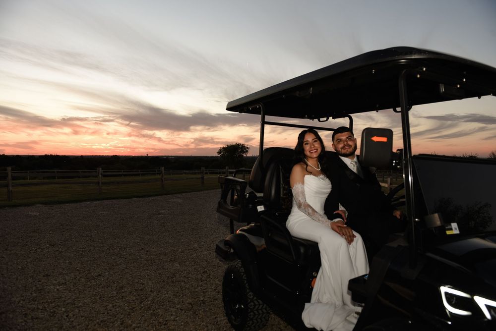 Bride and groom sitting together on a black golf cart at sunset during their outdoor wedding celebration.
