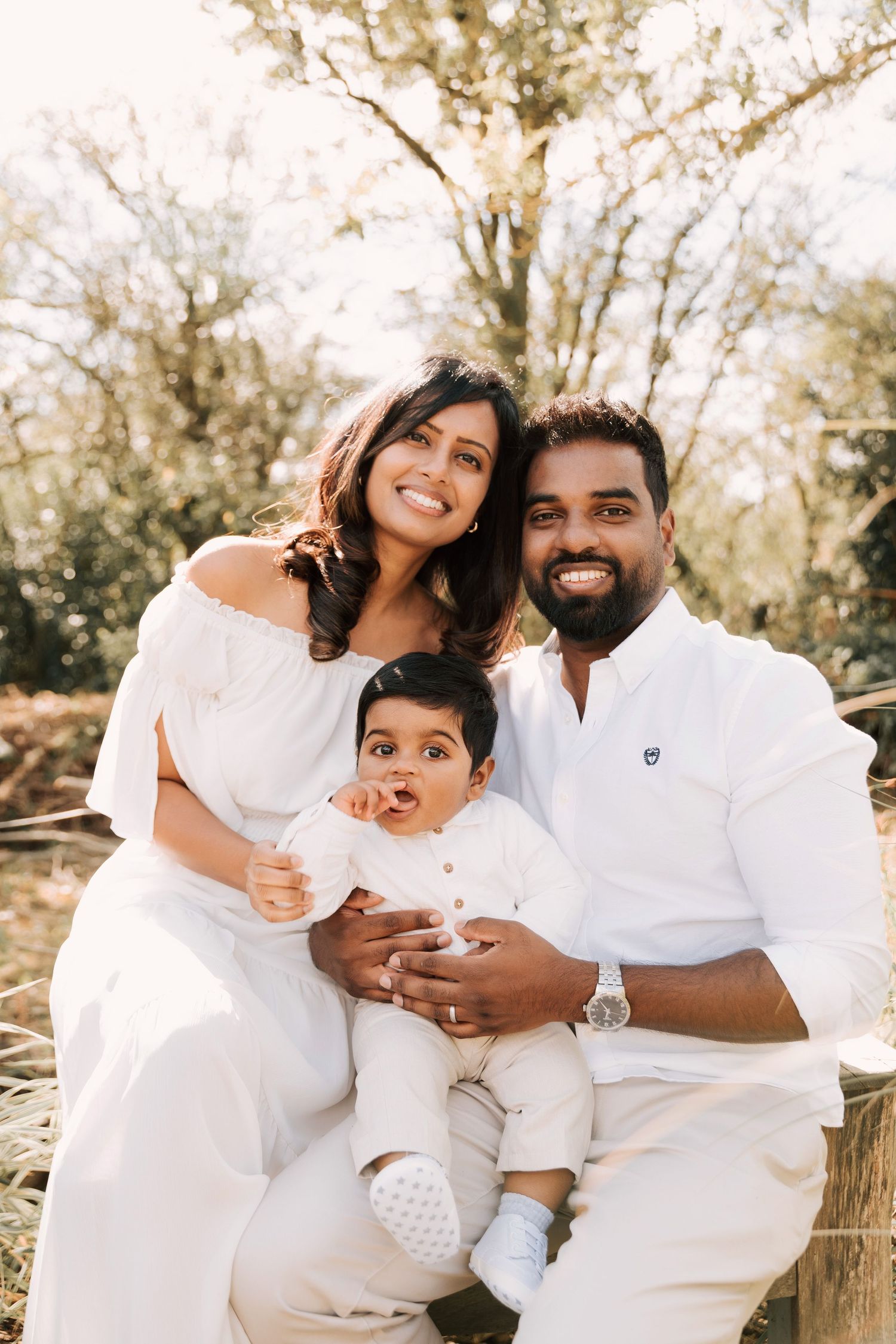 Family wearing coordinated white outfits poses together outdoors in natural setting during golden hour photoshoot.