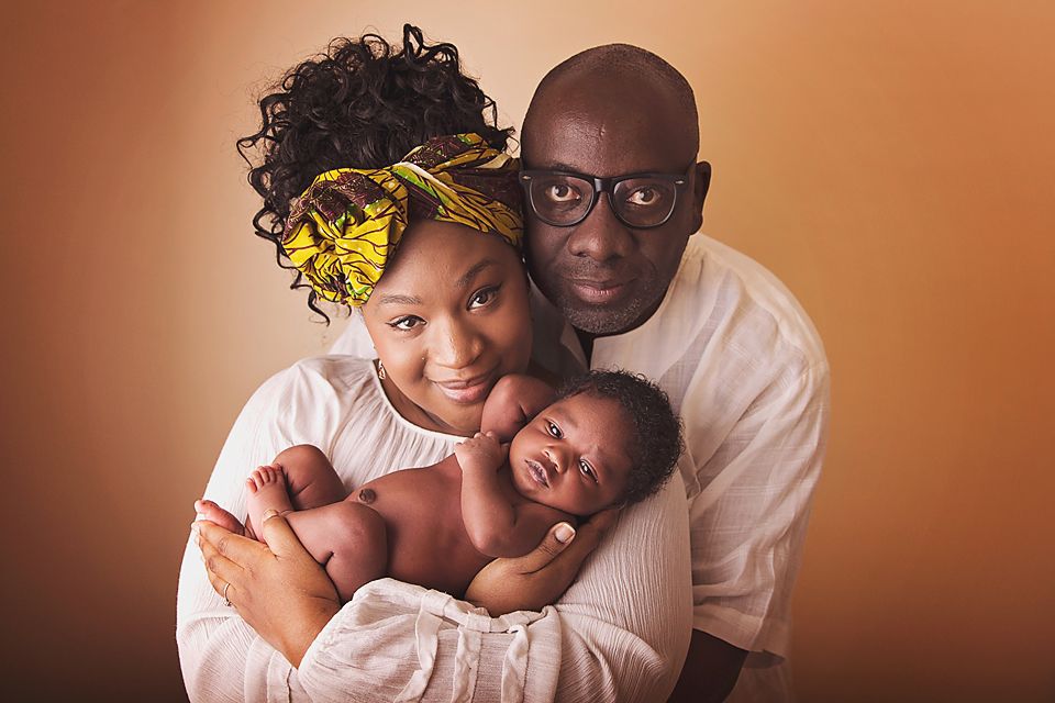 A loving family embraces while wearing white clothing against a warm brown background.