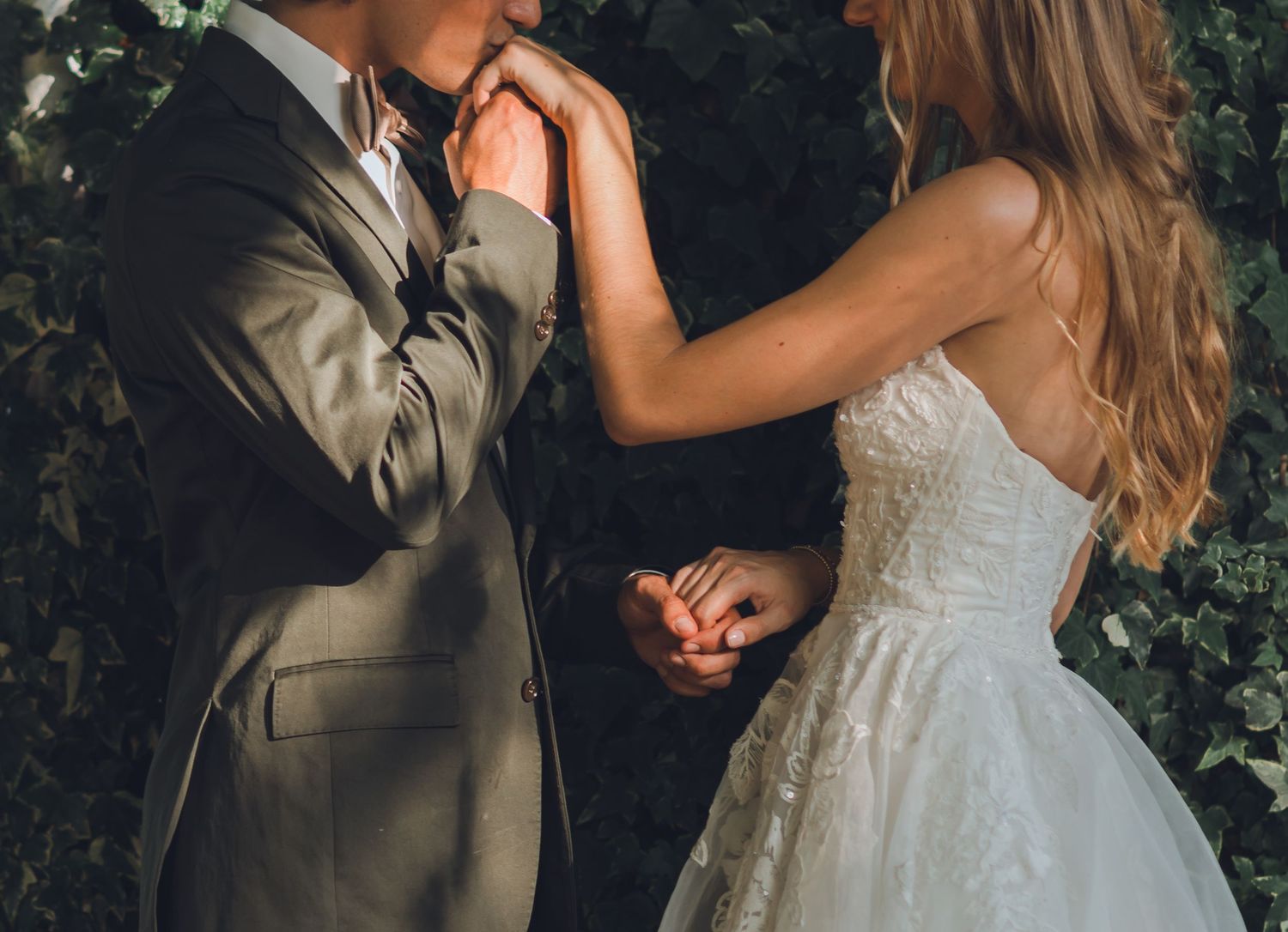 A couple in wedding attire share an intimate moment in a garden setting with lush greenery in the background.