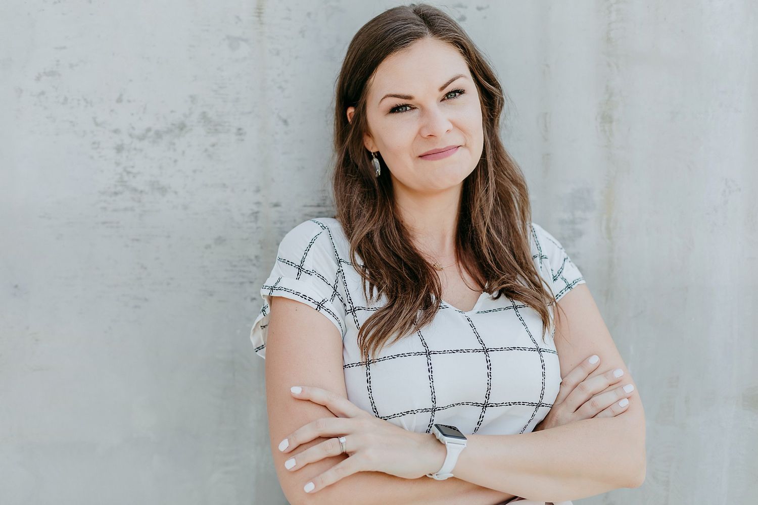 Woman in white windowpane dress poses against textured wall in a casual lifestyle photoshoot.