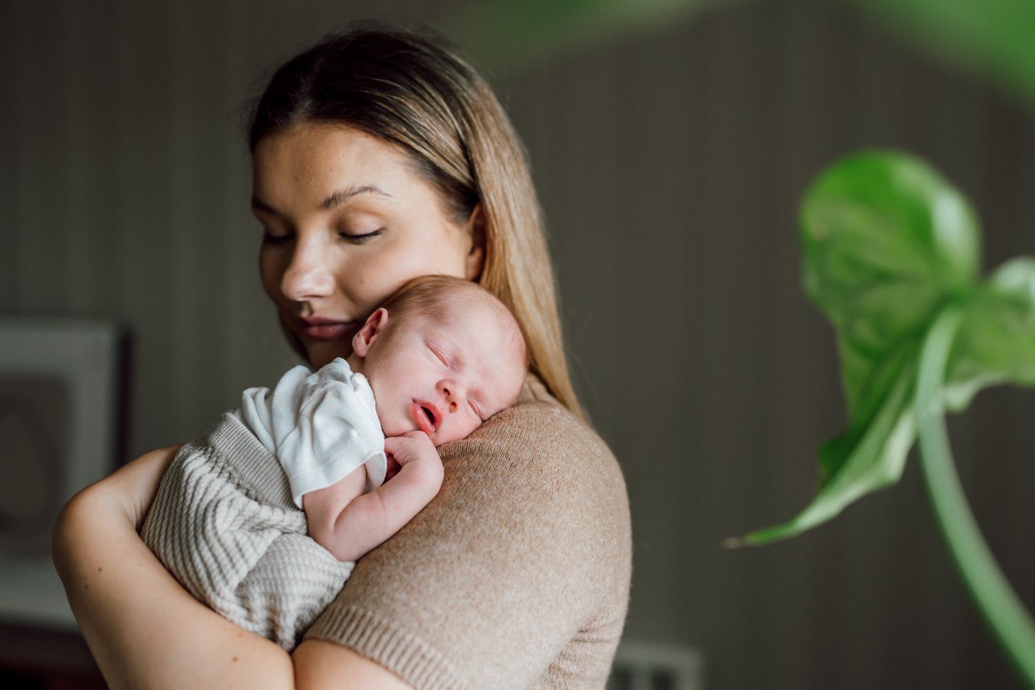 En liten bebis ligger på sin mammas axel under fotograferingen i hemmet.