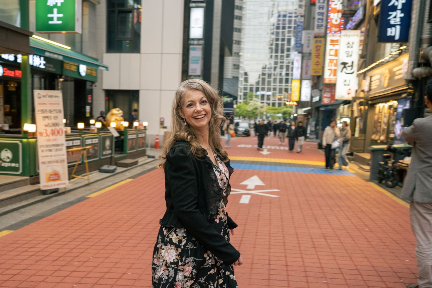 Person in black lace dress poses on red brick sidewalk in urban setting with city buildings in background.