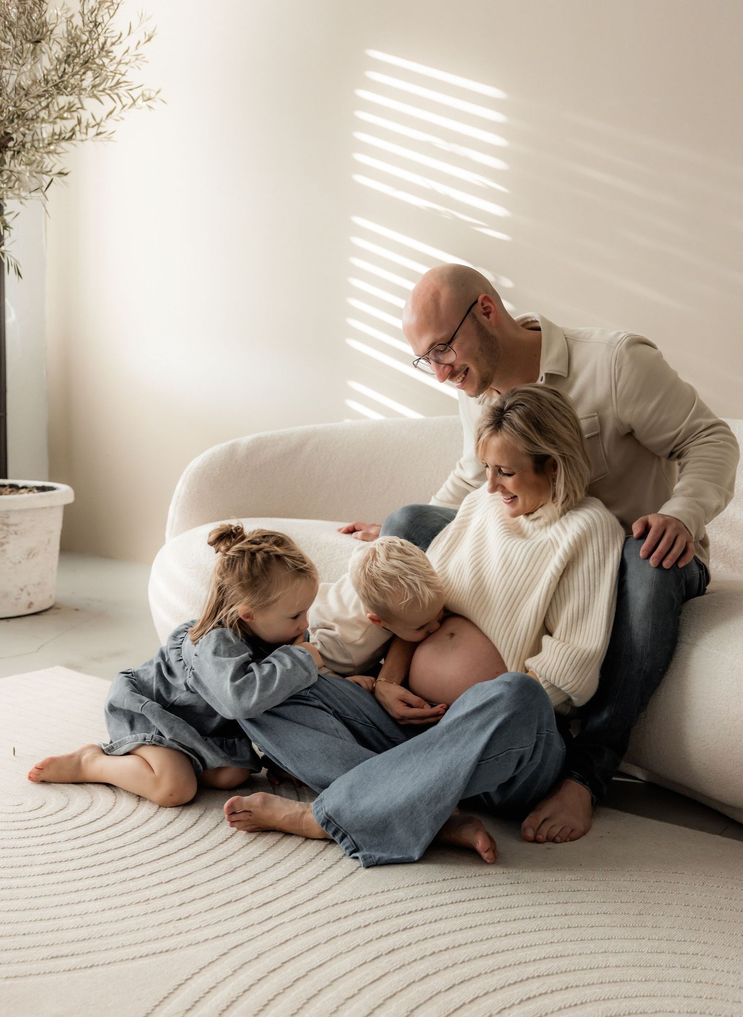Family lounging together on white carpet with sunlight streaming through window.