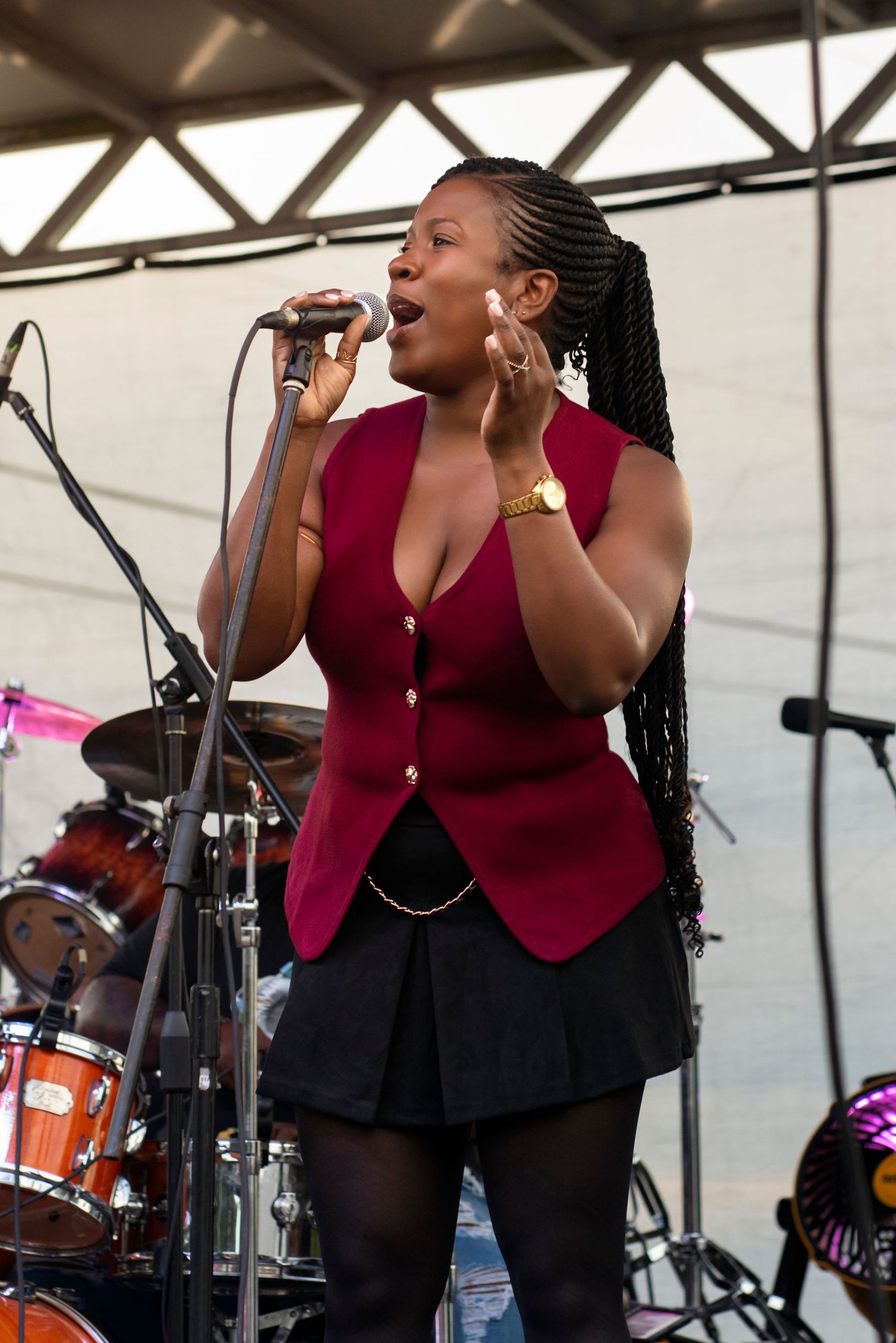 Three backup singers in burgundy outfits perform energetically on stage at an outdoor music festival.