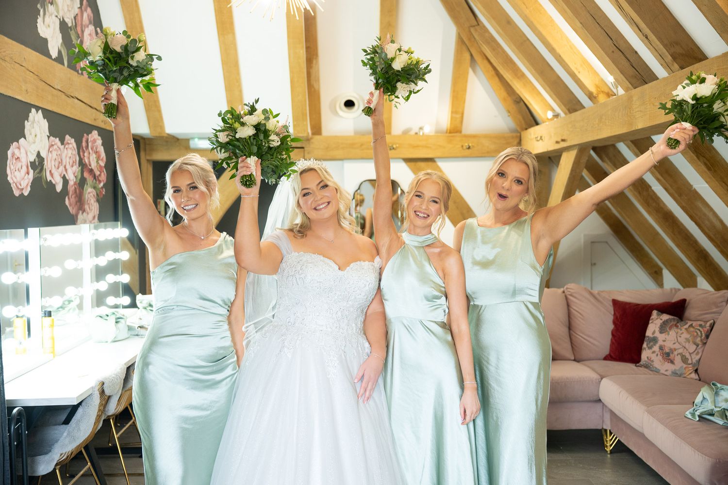 Bridesmaids in pale blue dresses stand together in a sunlit wooden beam venue.